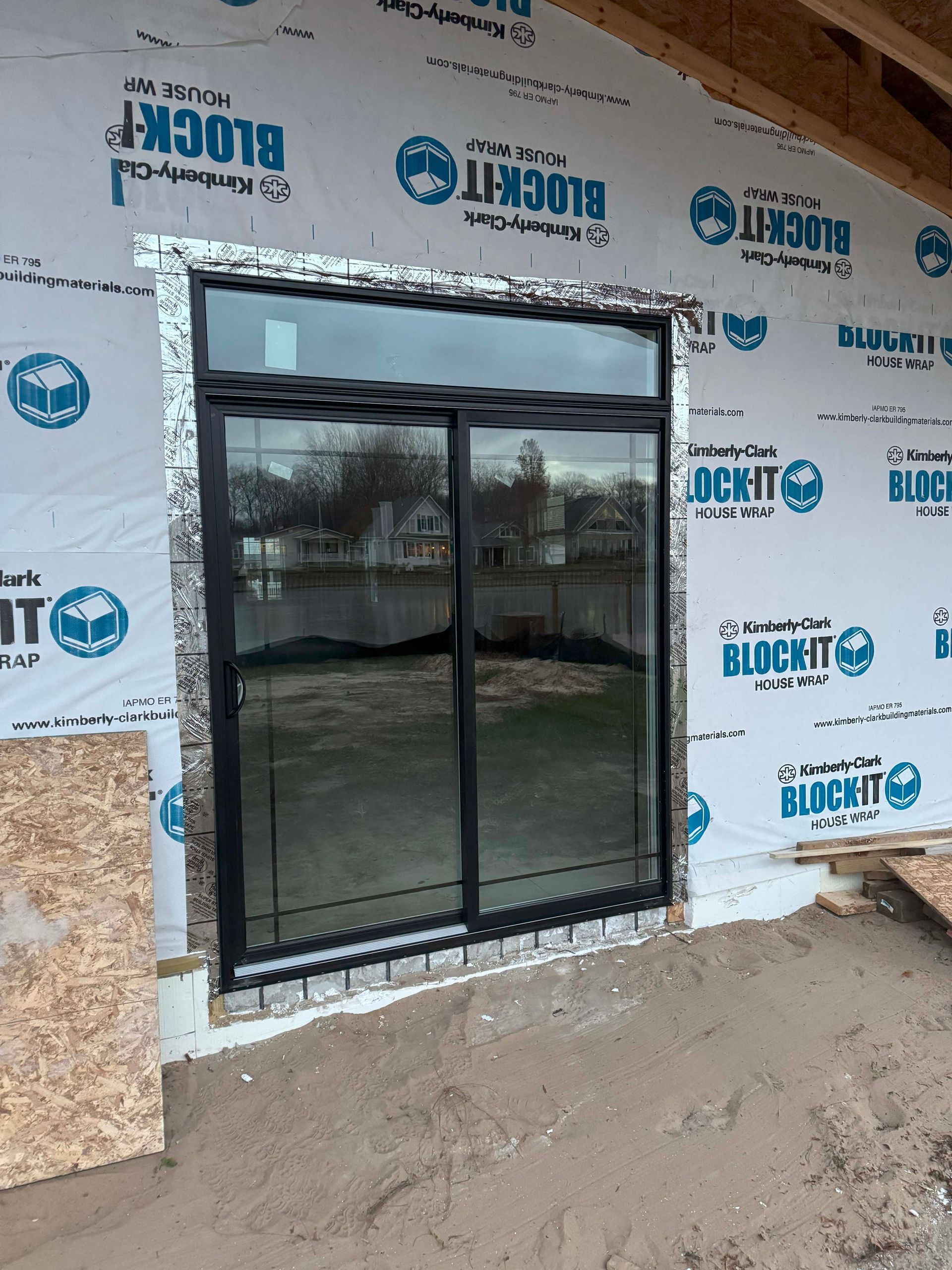 Black-framed sliding door in a building under construction, with sheathing and weatherproofing.