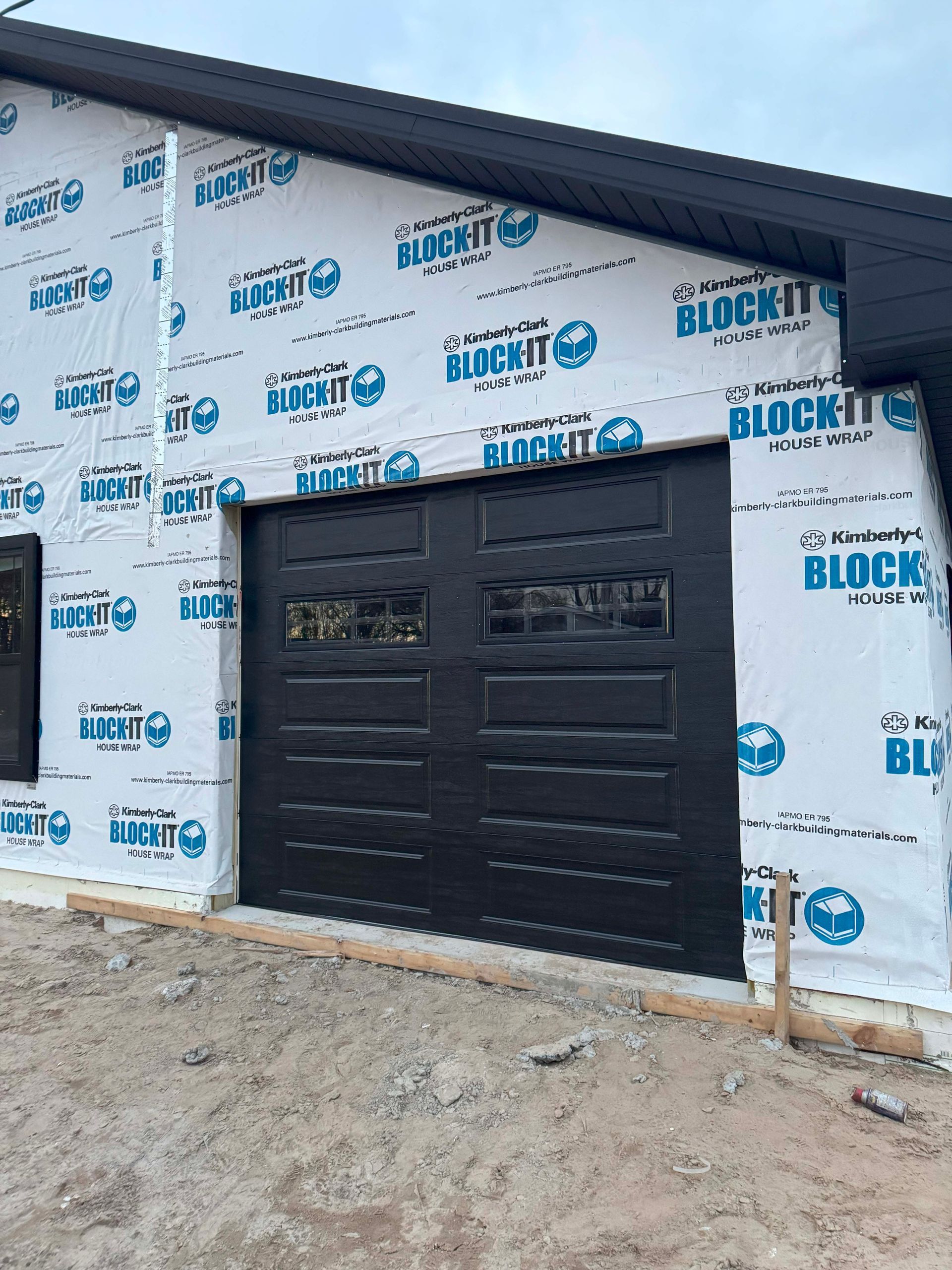 Black garage door on a new home under construction, covered in blue and white wrap.