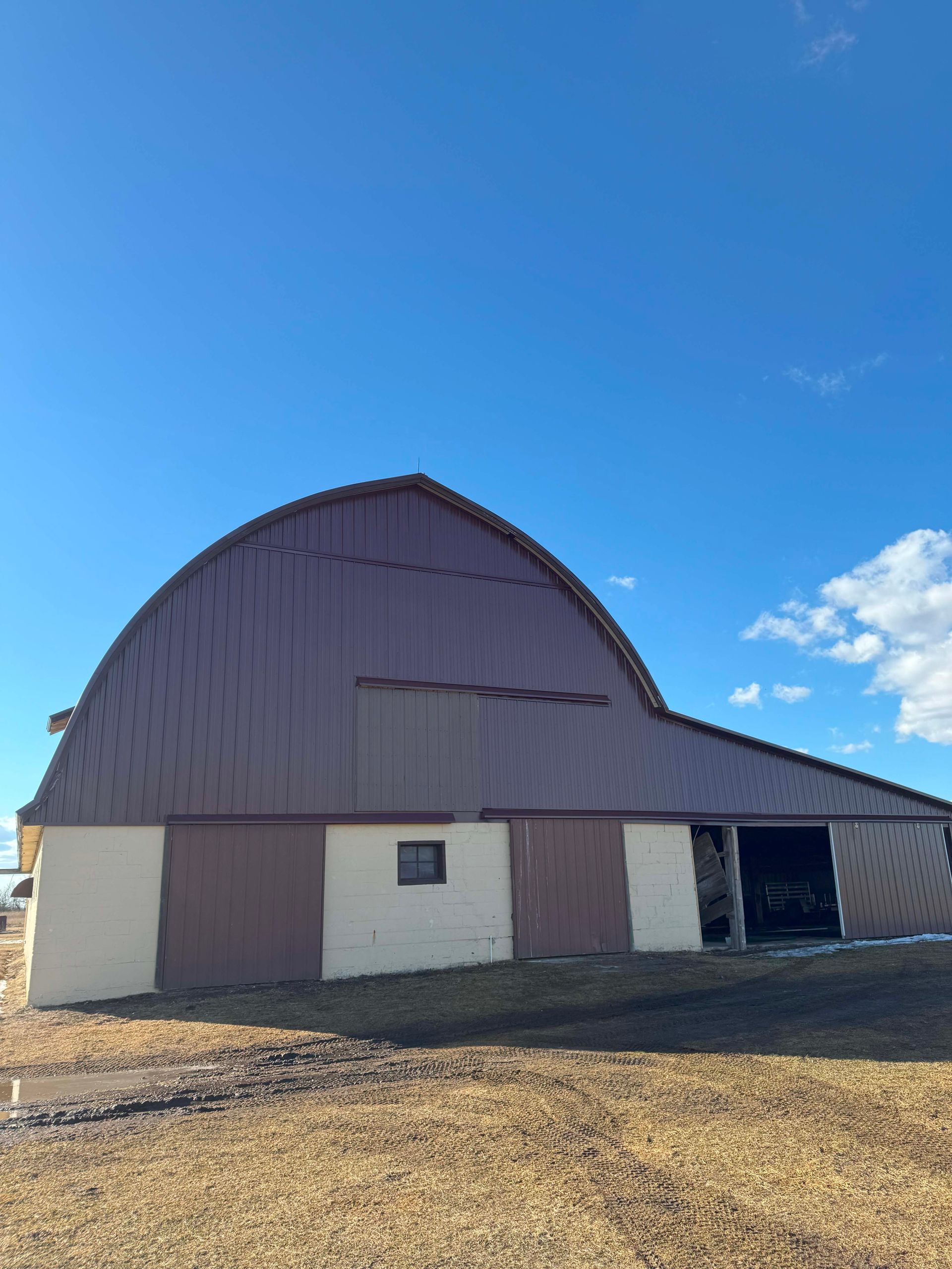 Brown Quonset barn under a bright blue sky.