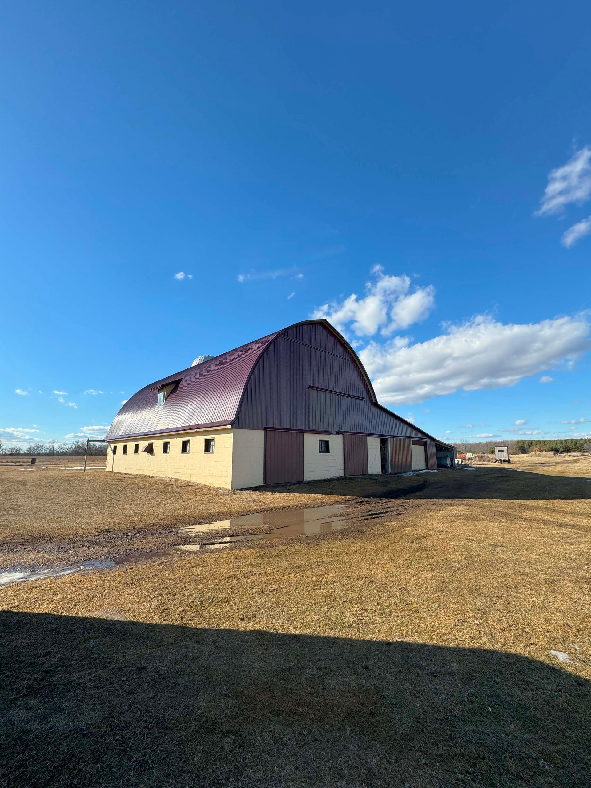 Red roof barn under blue sky; beige walls.