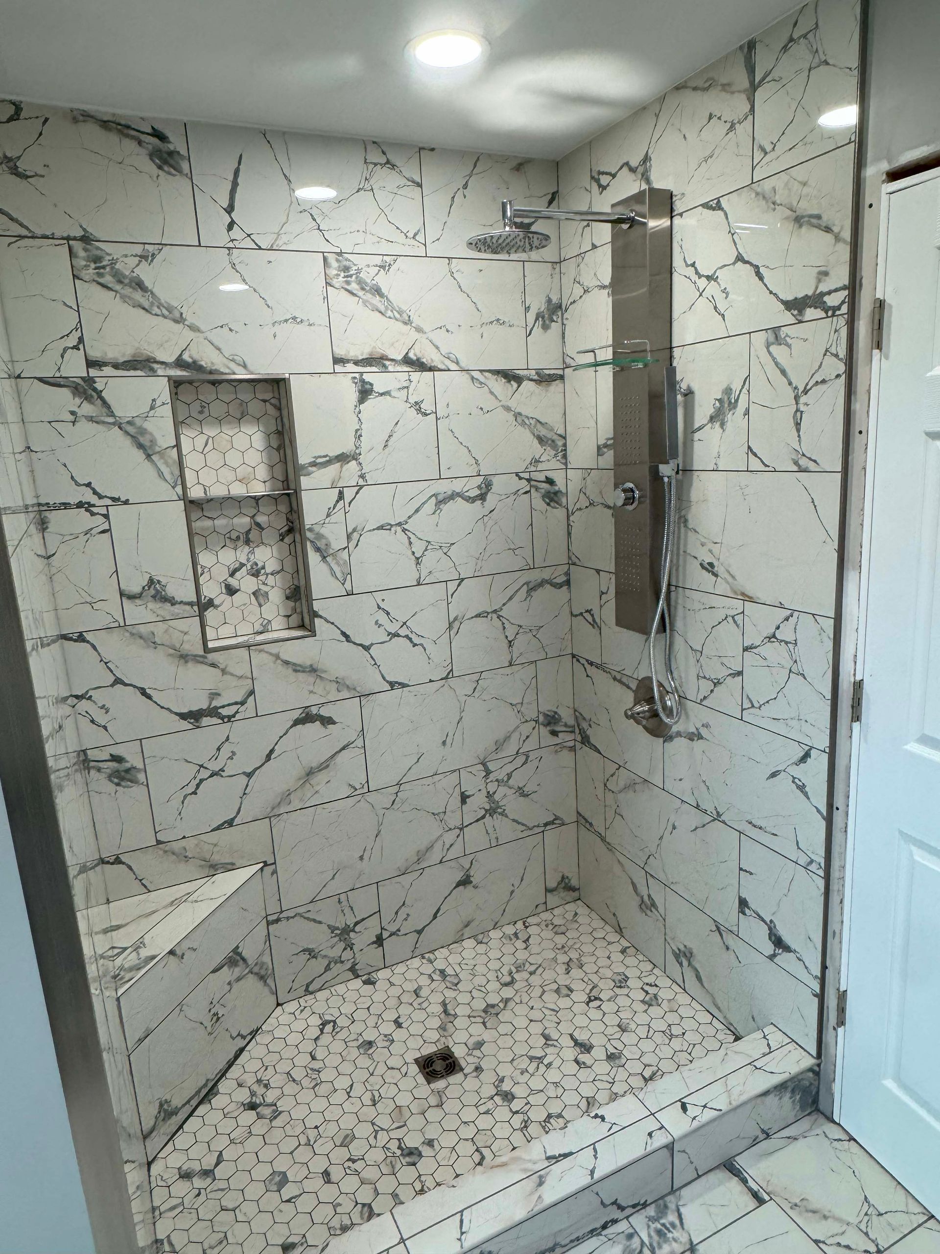 Modern shower with marble-look walls, built-in shelf, and a bench.