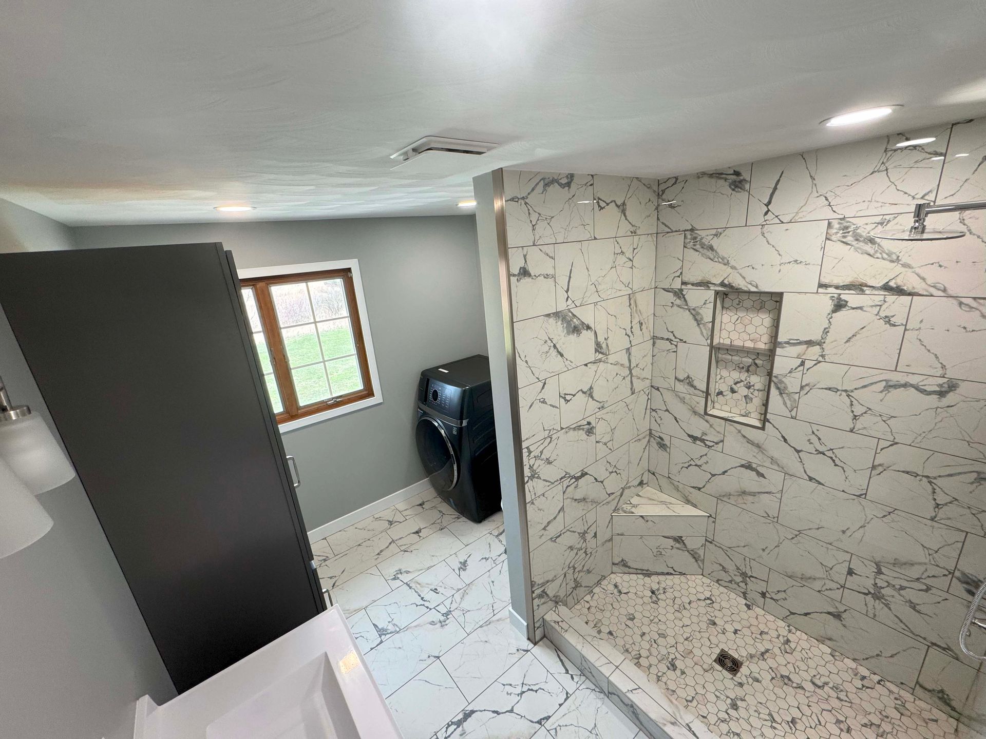 Bathroom with marble shower, washing machine, and gray walls.