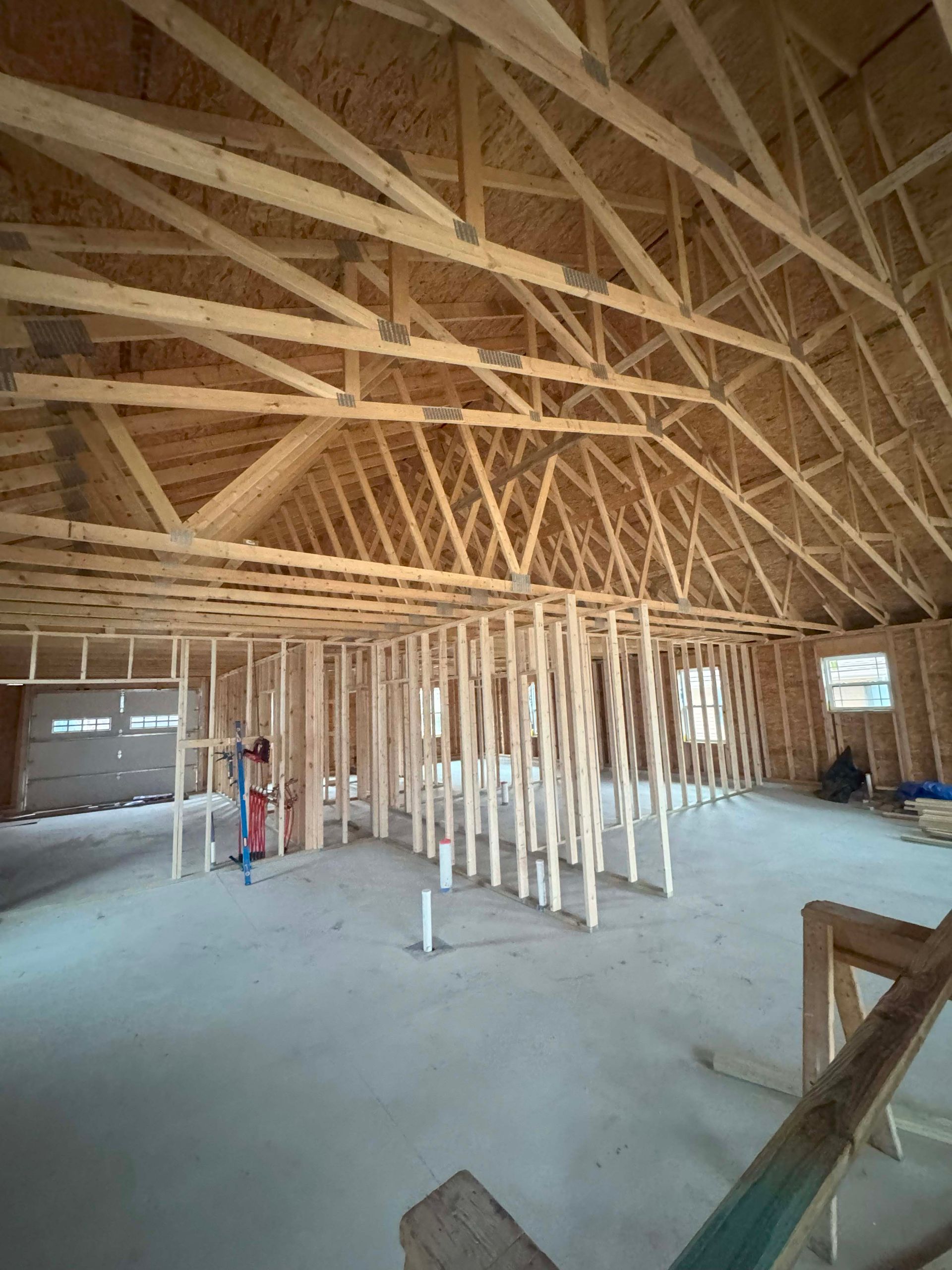 Interior view of a building under construction, with exposed wooden rafters, framing, and concrete floor.