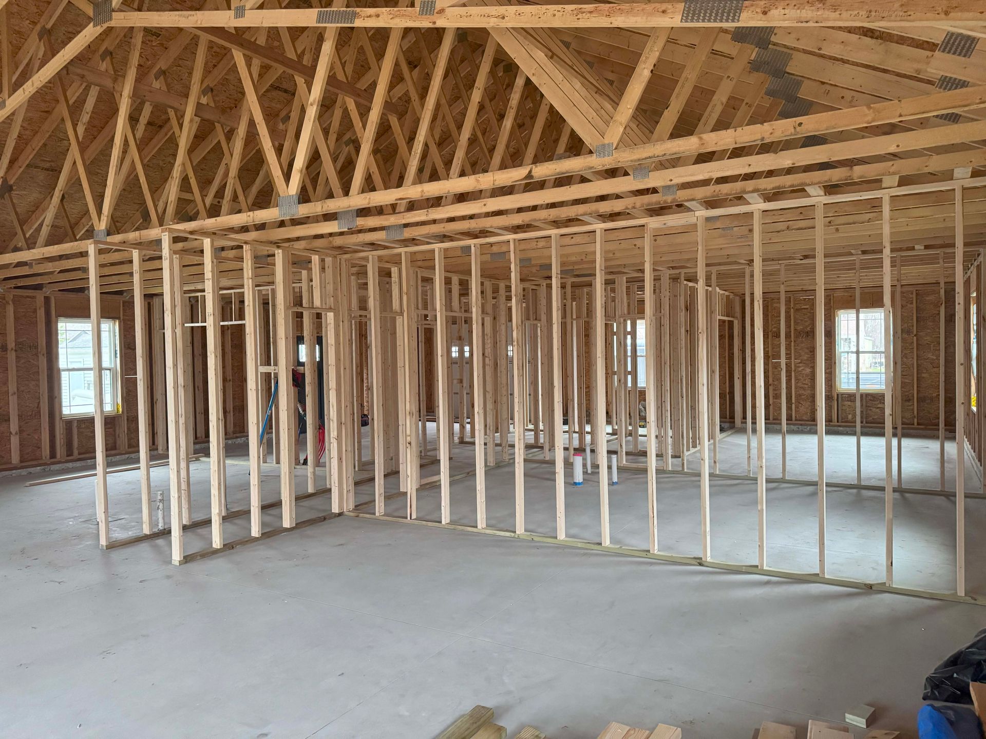 Interior view of a building under construction, showing wooden framing for walls and roof, with concrete flooring.