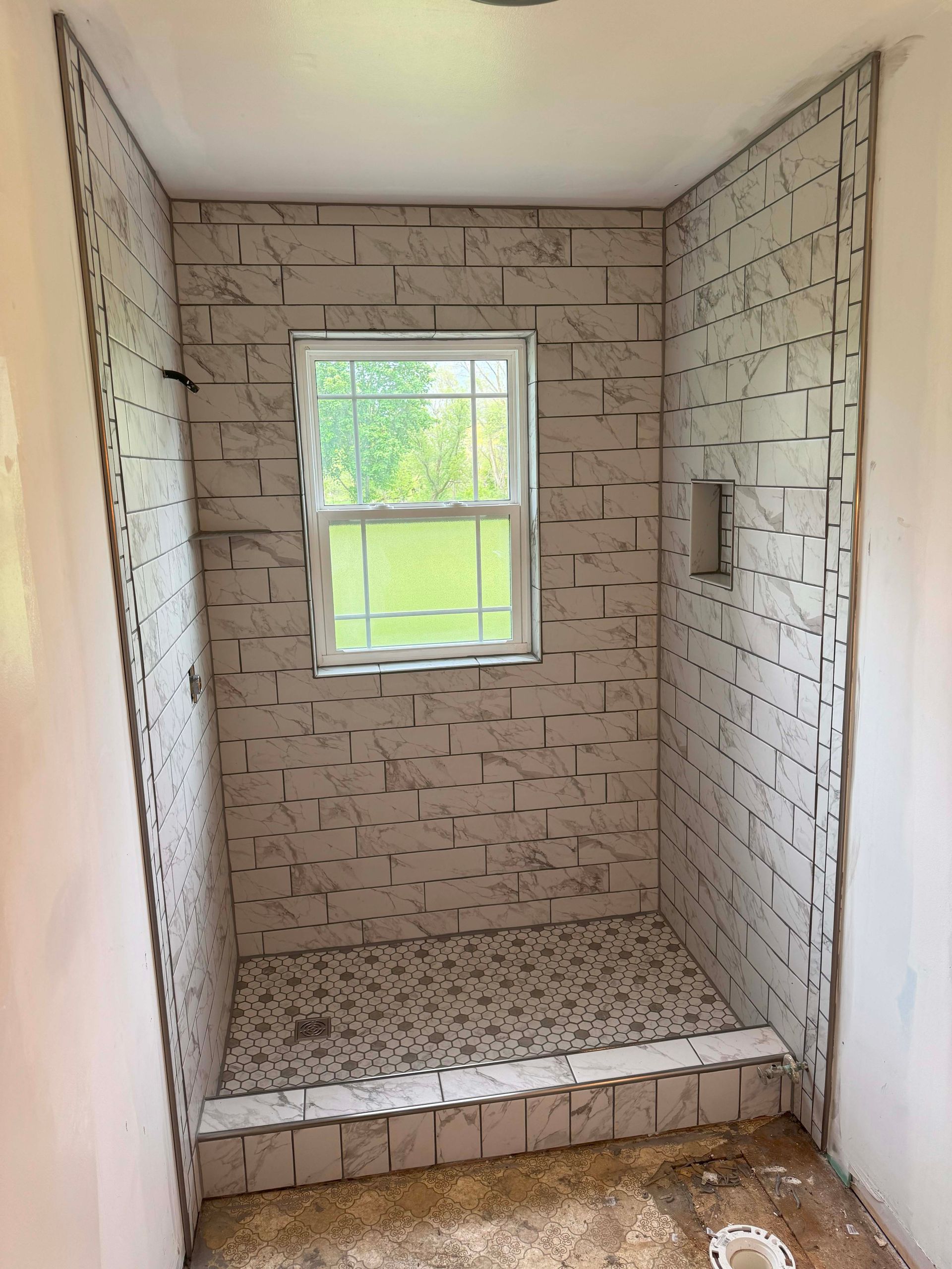 Shower stall under construction, with tiled walls, window, and low threshold.