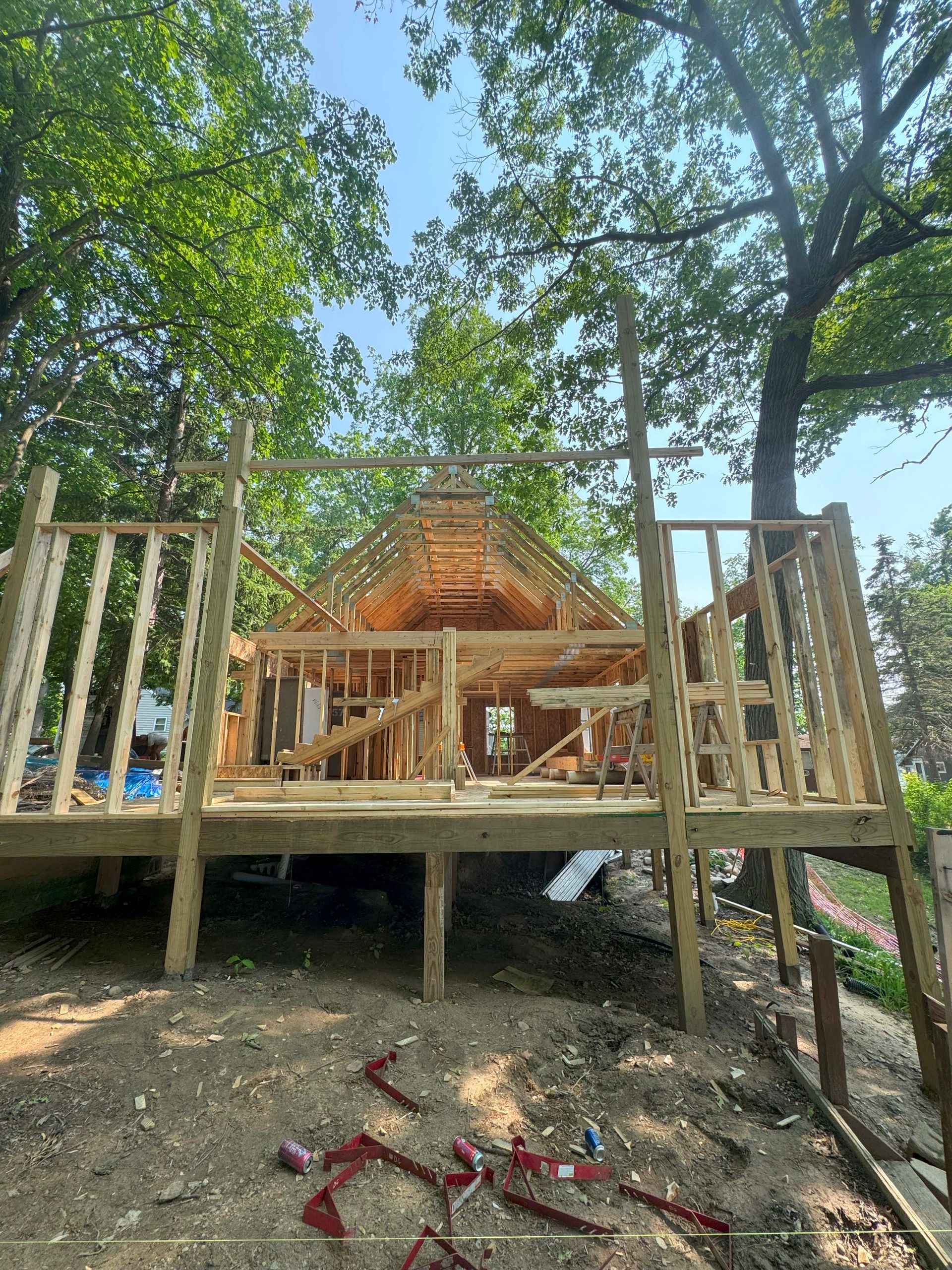 Wooden cabin under construction with deck; trees in background.