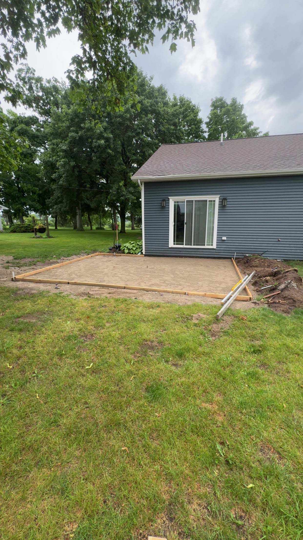 Backyard with gravel patio, adjacent to a blue house with a sliding glass door. Green grass surrounds.