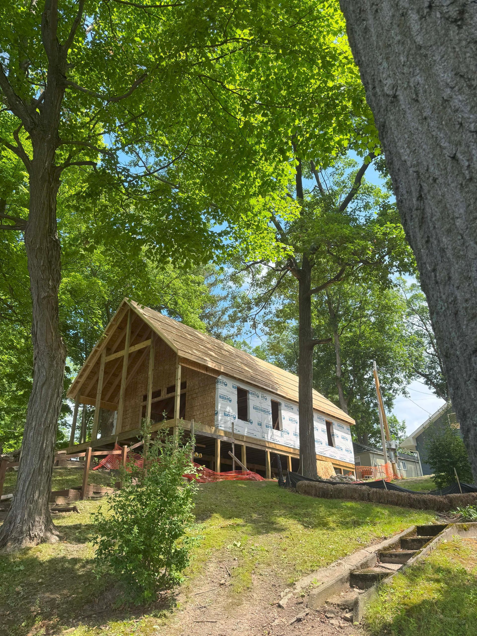 Construction of a wooden building, surrounded by trees and grass, under a blue sky.
