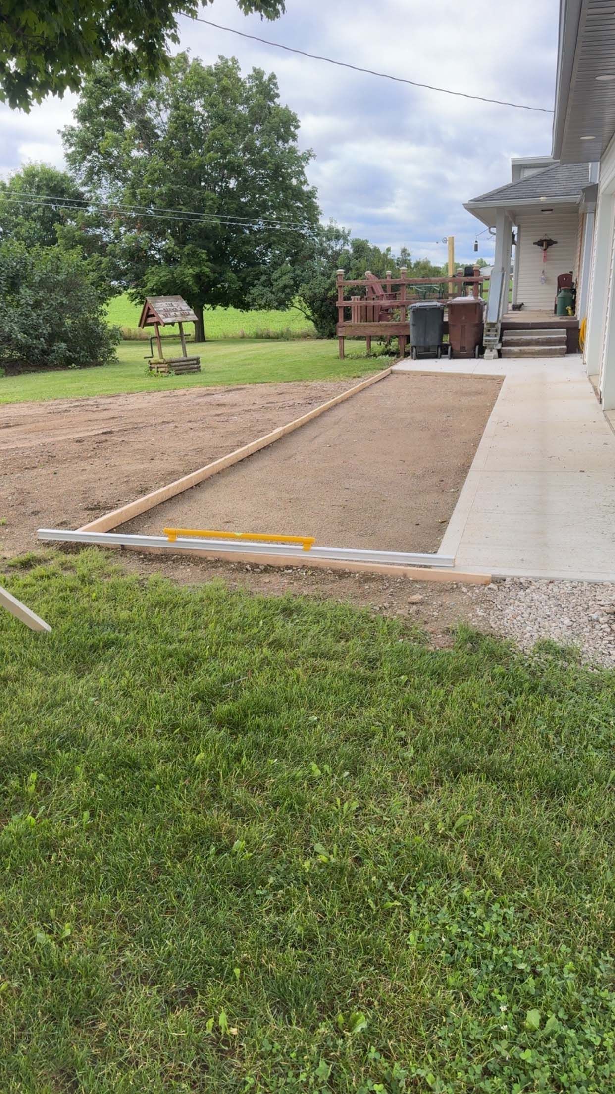 Yard construction: Gravel and leveled soil next to a concrete walkway and green grass.