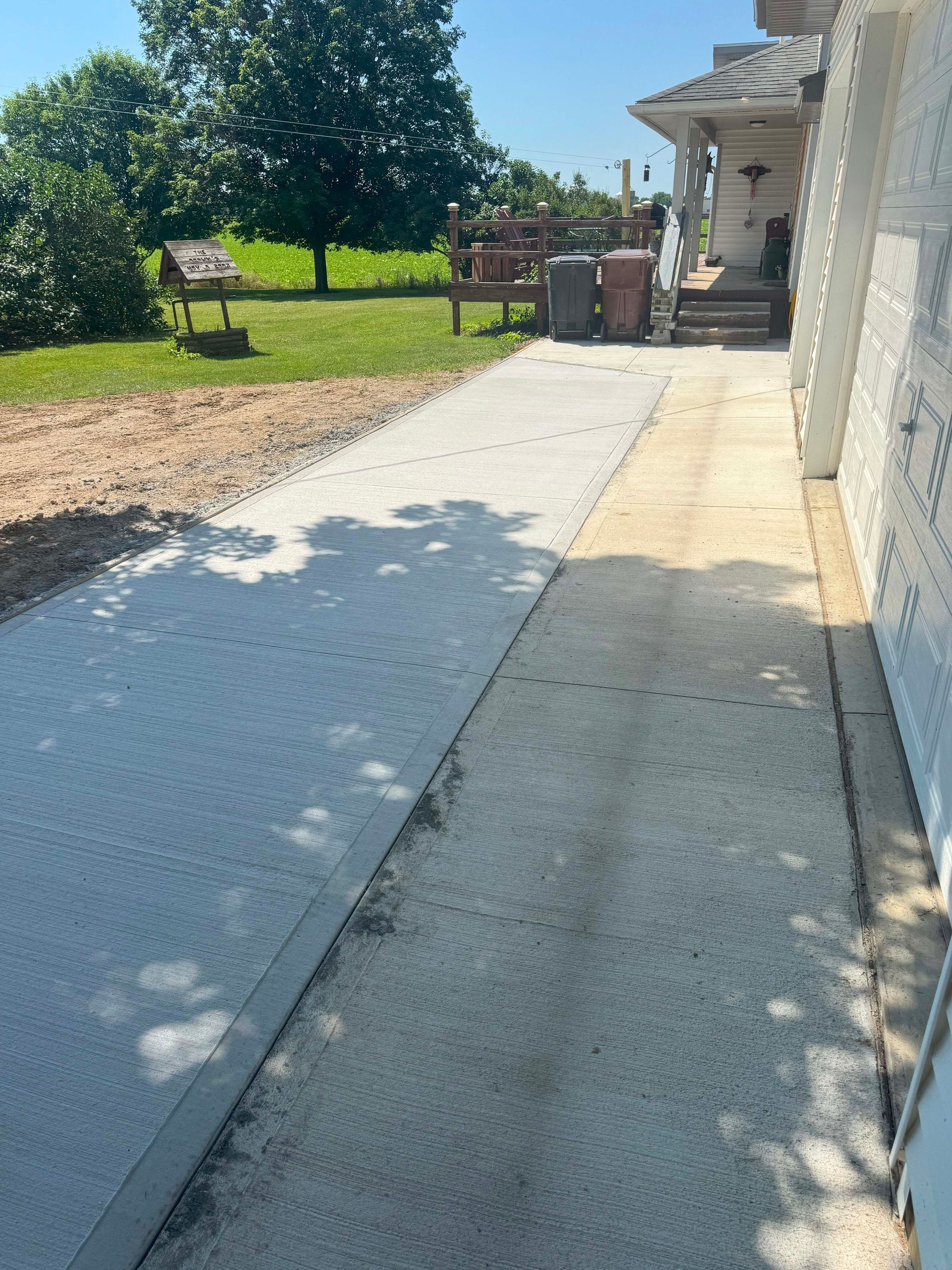 Concrete pathway leading to a house, with a textured and a smooth section. Sunny day.