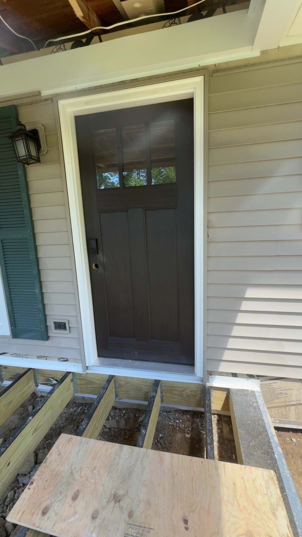 Brown front door with white trim and a partially built wooden porch.