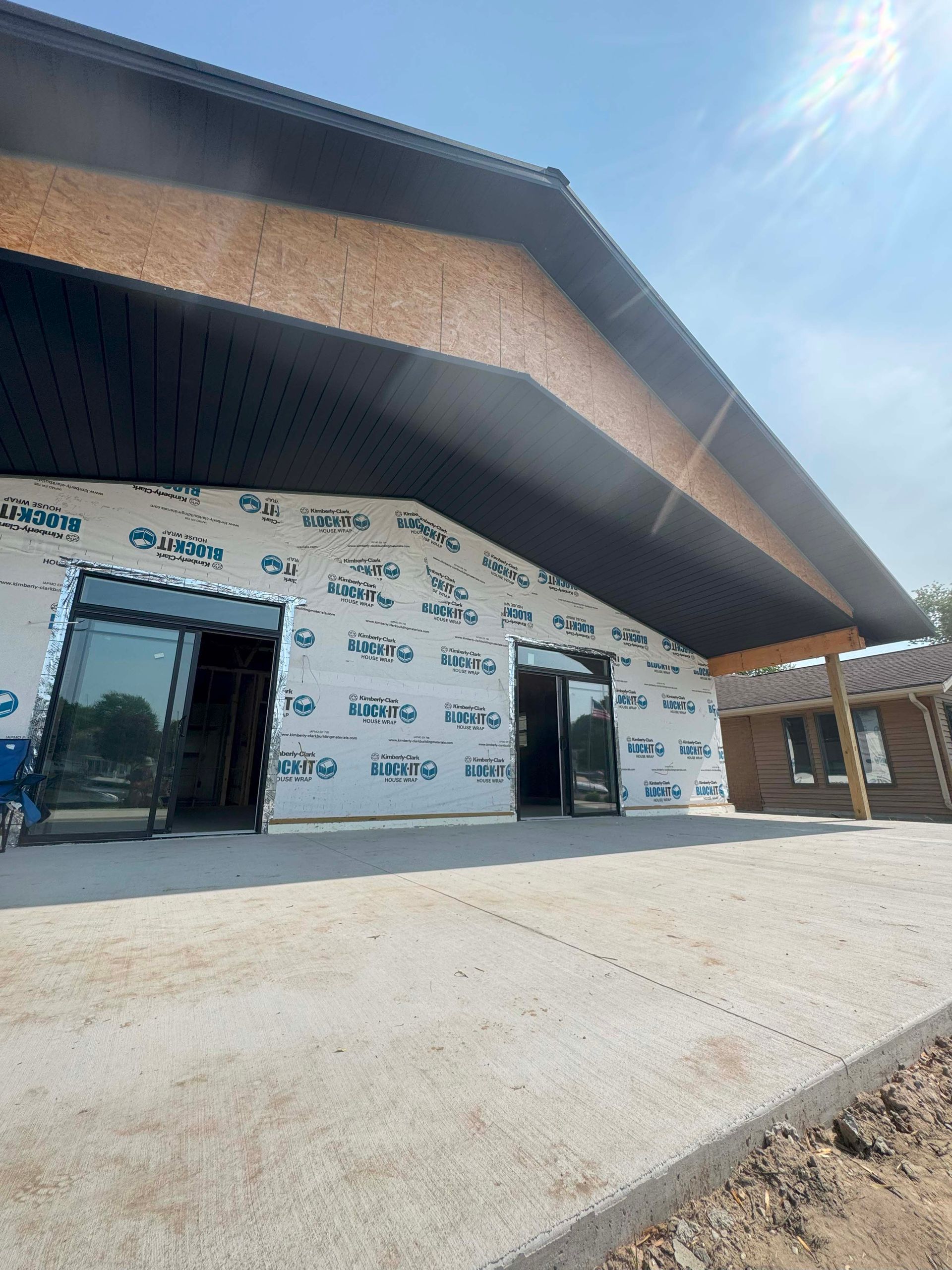 Building under construction with black roof, glass doors, and concrete patio.