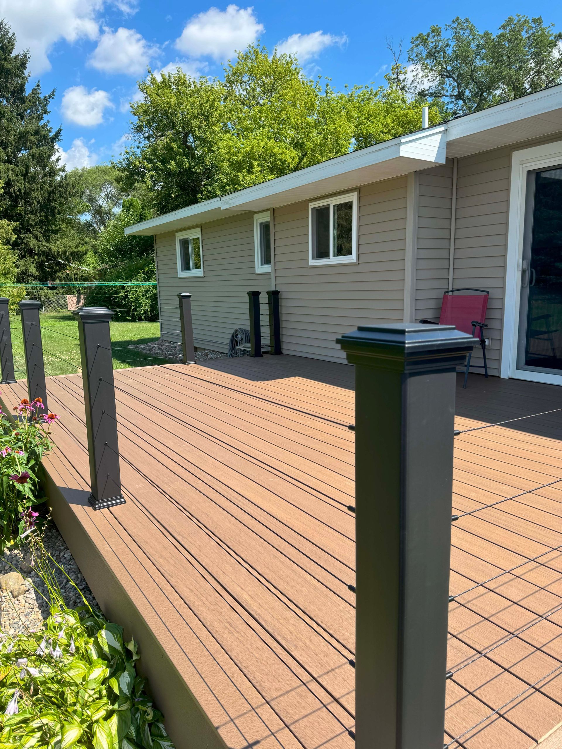 Composite deck with dark brown boards and black railing posts, next to a beige house with a green yard.