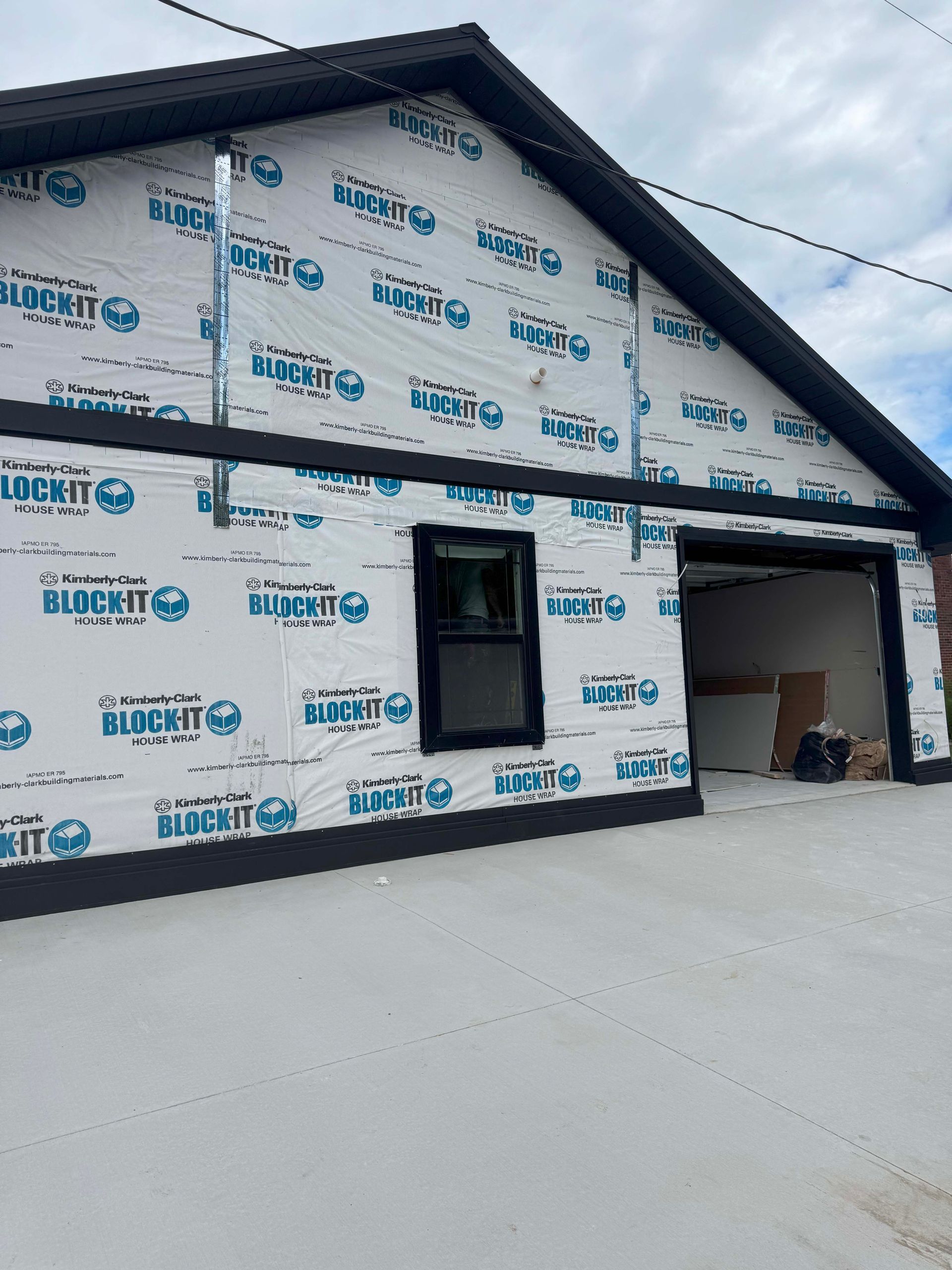 Garage under construction with white house wrap, black trim, and open garage door.