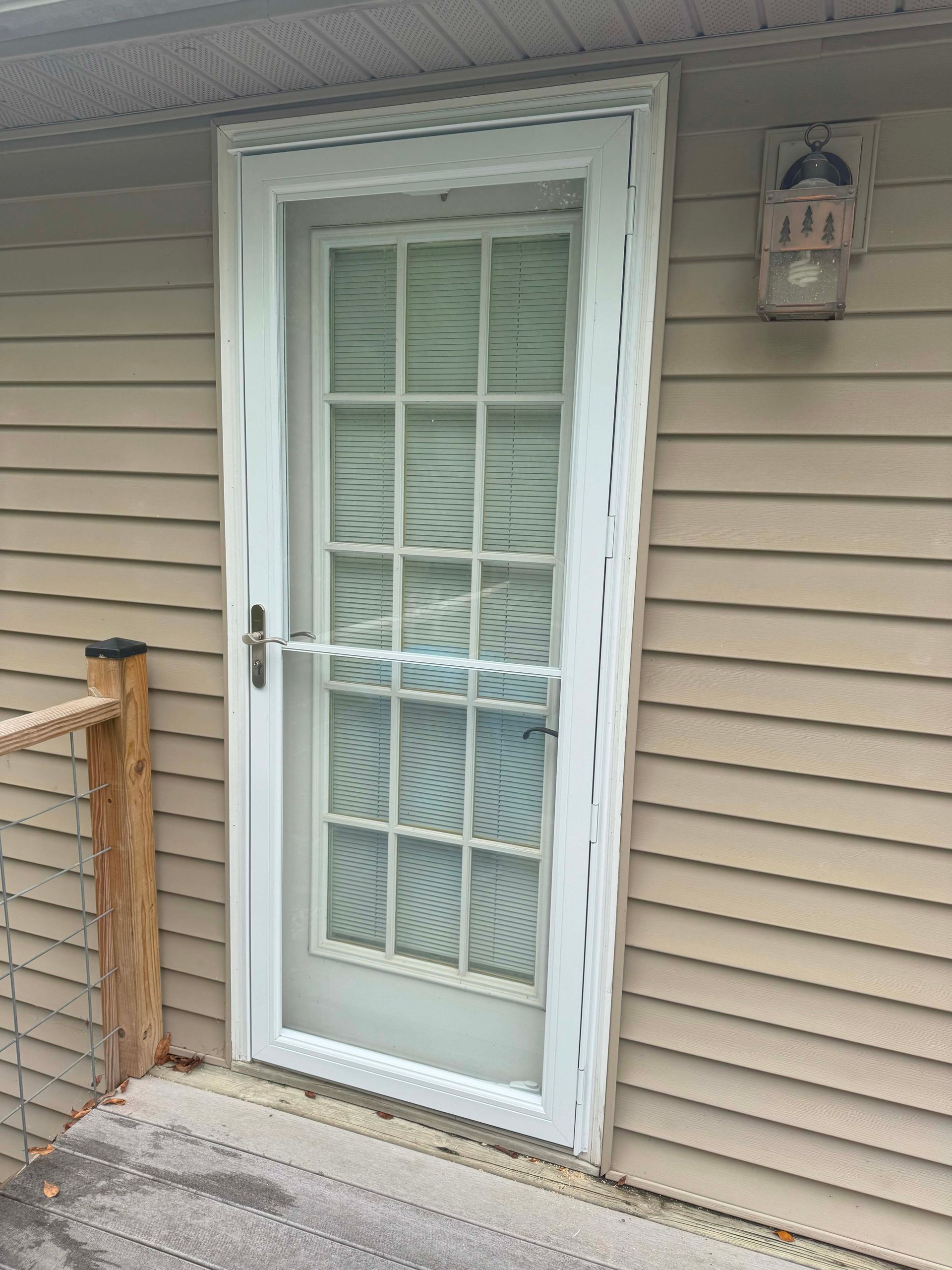 White screen door with grid pattern on a beige siding exterior. Security camera is mounted on the wall.