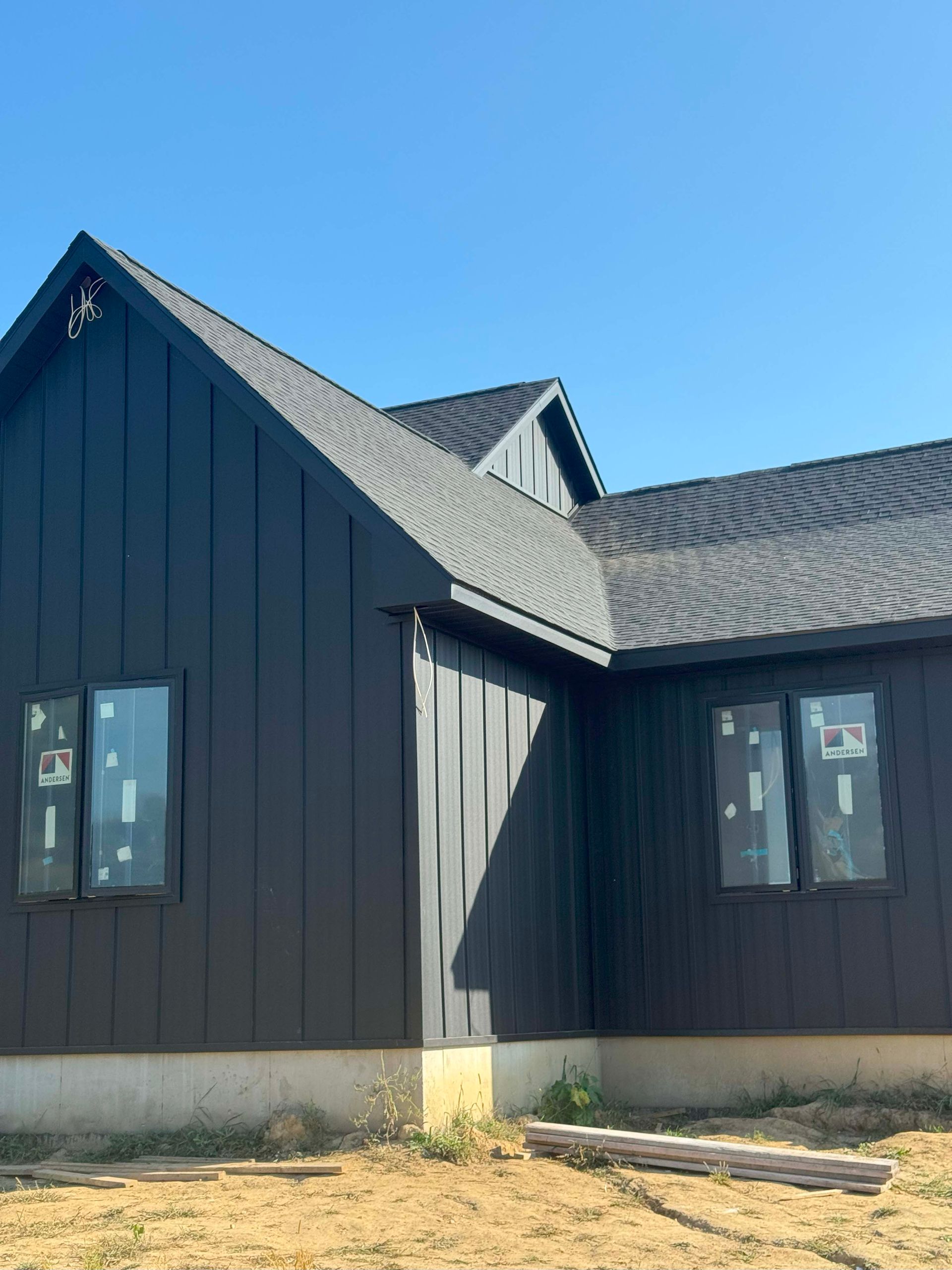Black house with dark roof and trim, two windows, set against a blue sky.