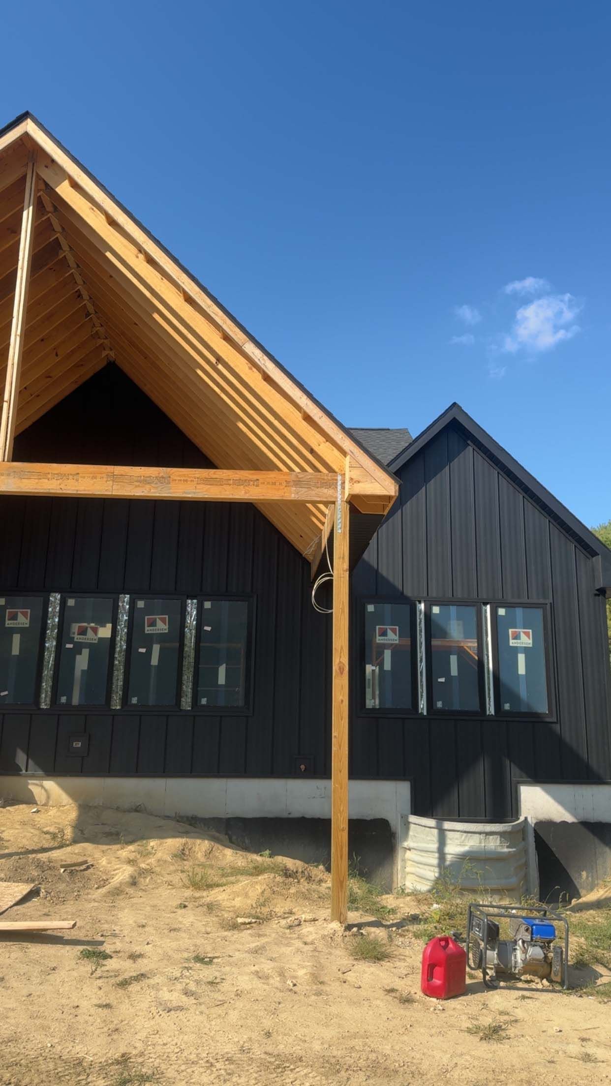 Black-clad house under construction with exposed wooden beams, multiple windows, and a bright blue sky.