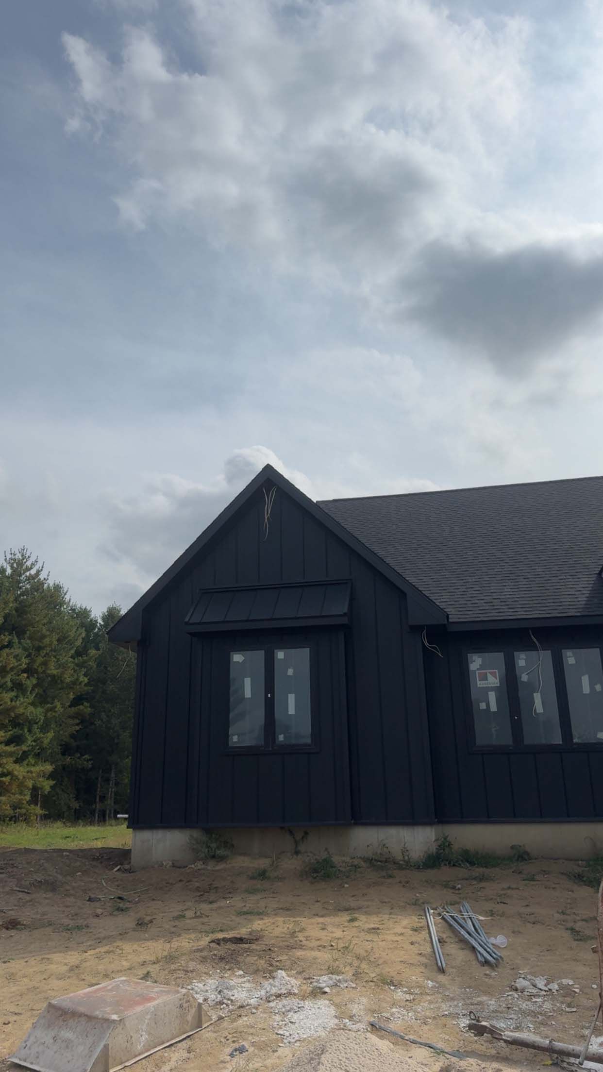 Black modern house under cloudy sky; windows, dark wood exterior.