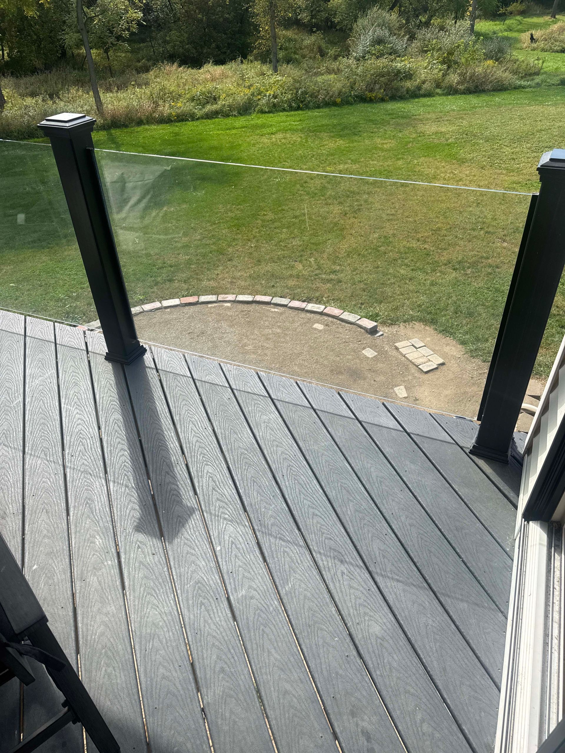 Gray composite deck with glass railing overlooks a grassy yard.