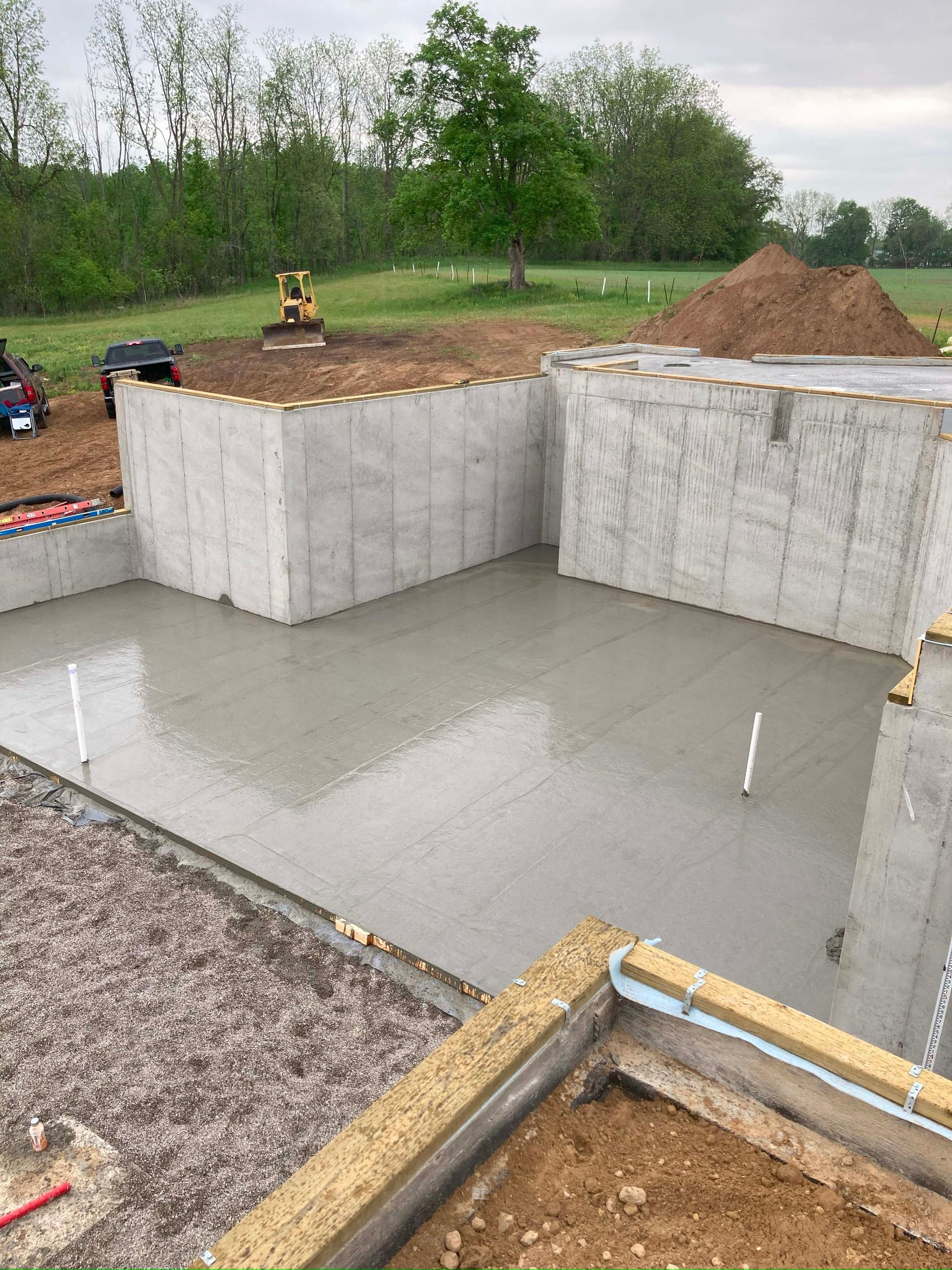 Concrete foundation poured for a building; walls and floor are gray, construction setting outdoors.