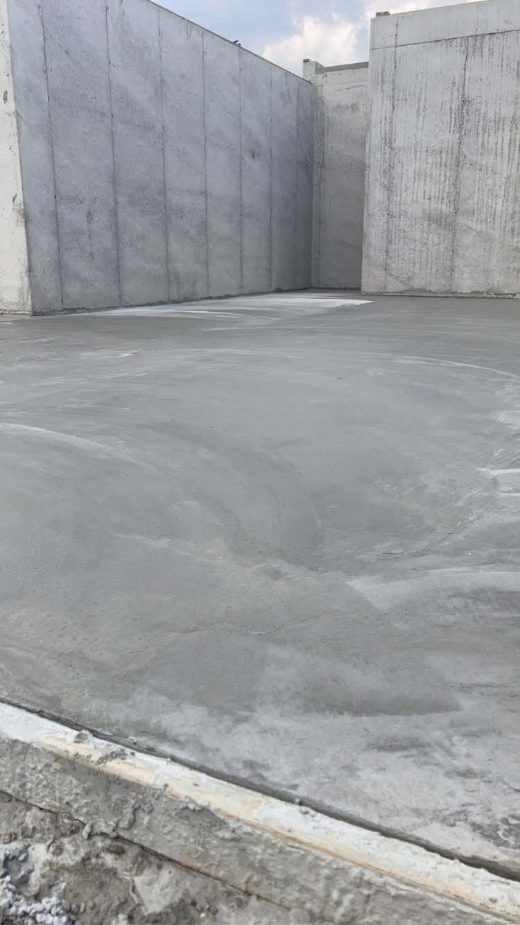 Concrete floor in a large gray walled space, recently poured.