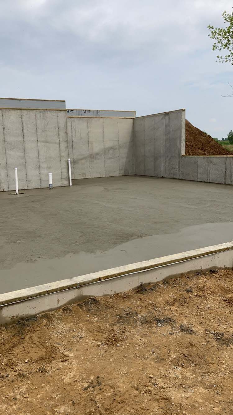 Concrete foundation of a building under construction, with gray walls and freshly poured concrete floor.