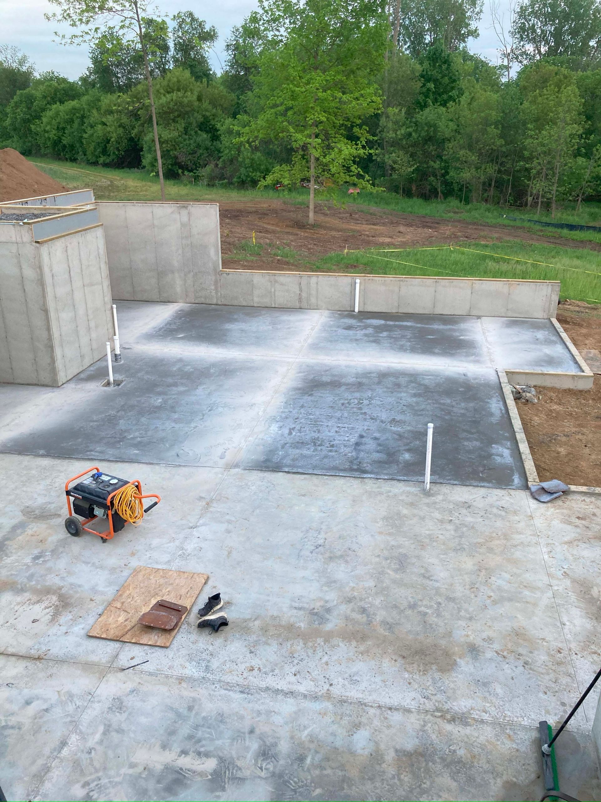 Concrete patio under construction with cement walls, power washer, tools, and grass in background.