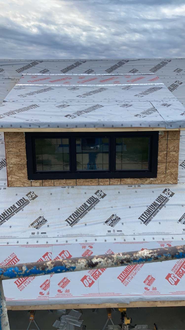 Window installation on a roof, surrounded by sheathing and underlayment.