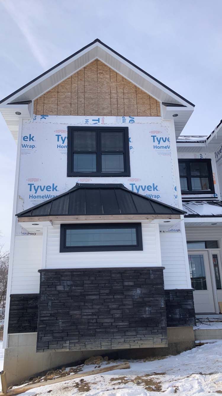 Two-story house under construction, with black trim windows, a black stone facade, and Tyvek wrap.