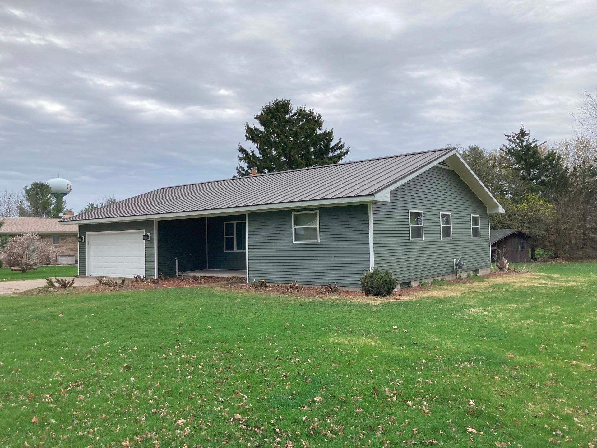 Green house with wavy siding, white garage door, cloudy sky.