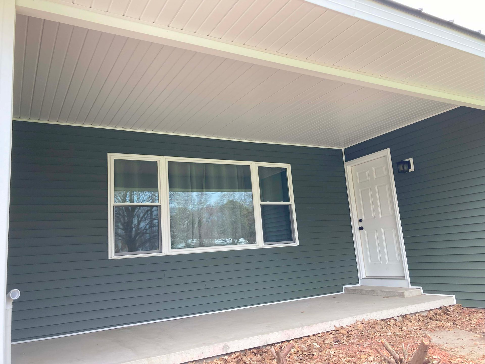 Exterior of a house with teal siding, white trim, and a concrete porch under a covered area.