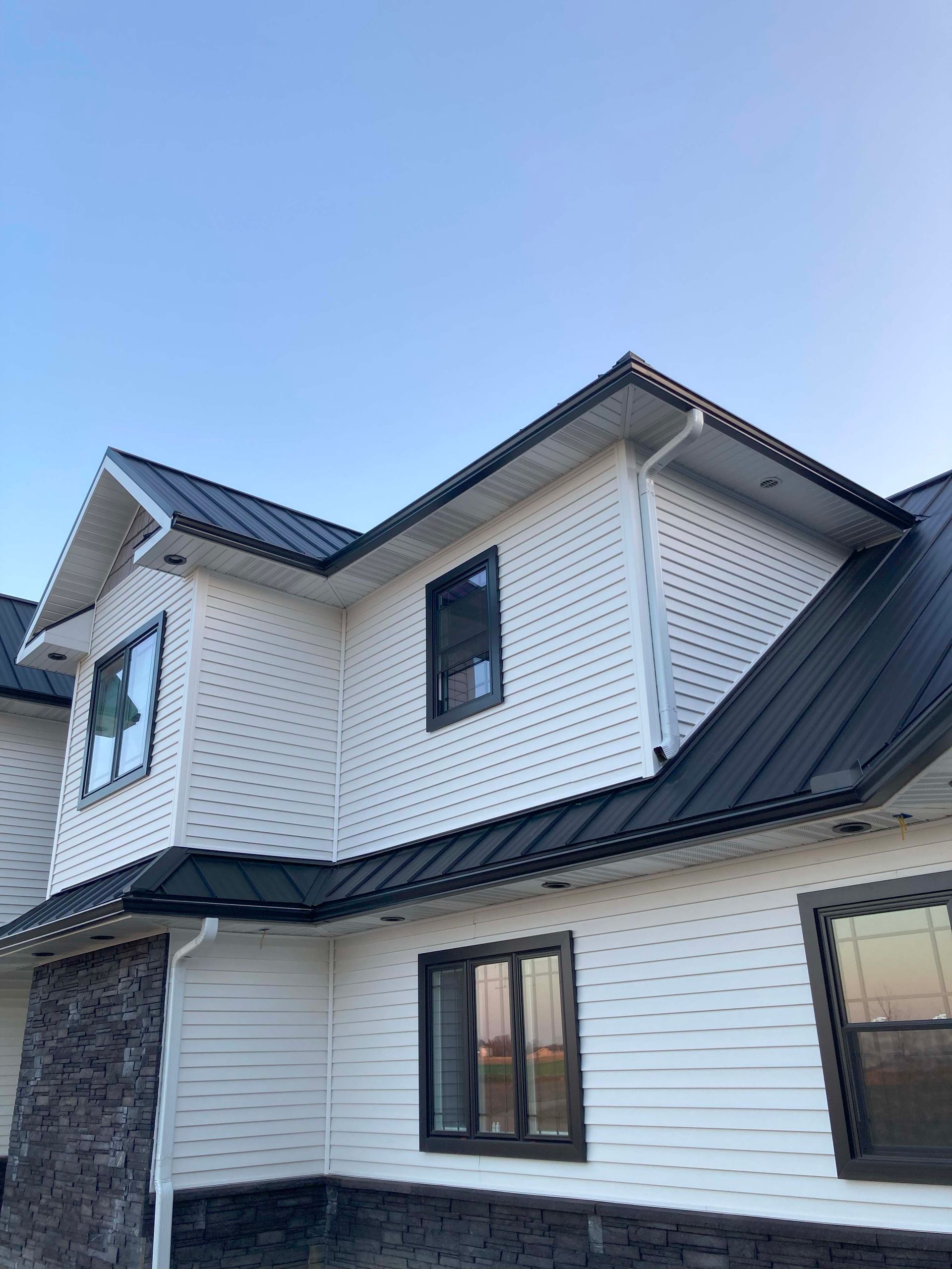 White house with black metal roof and trim, dark windows, and stone accents.