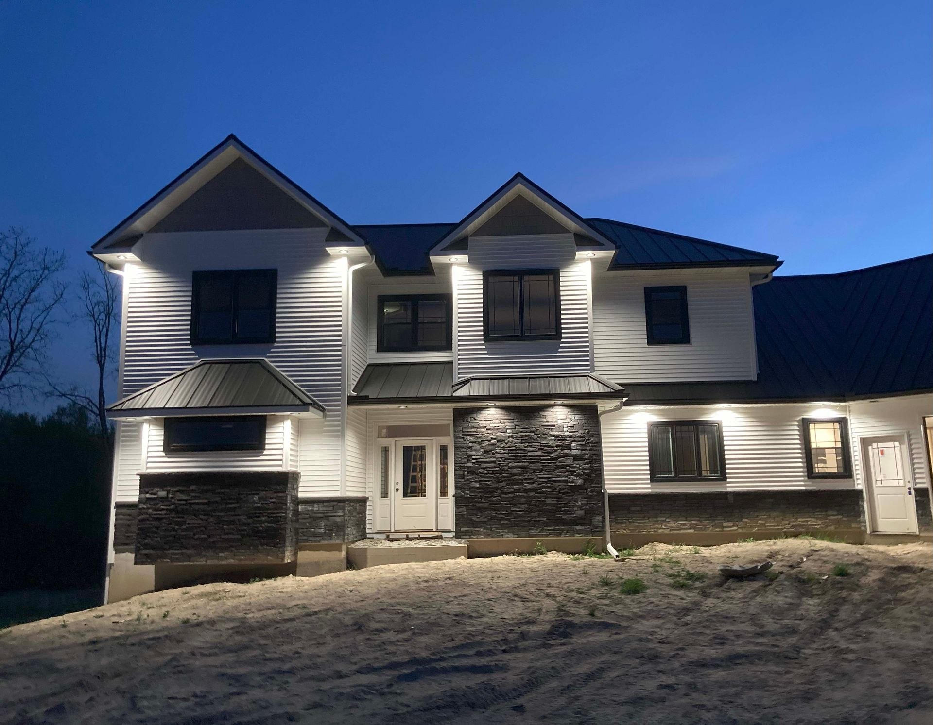 Two-story white house with black roof and stone accents, illuminated at dusk.