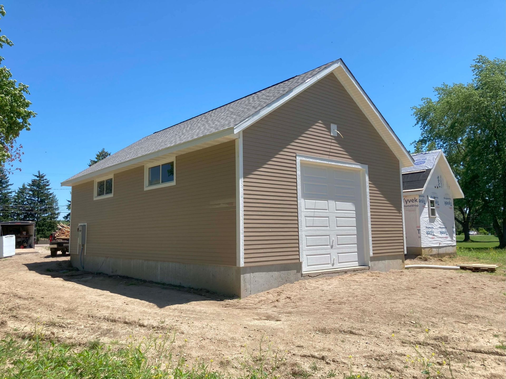 Tan building with white garage door and windows under a blue sky, on a dirt lot.