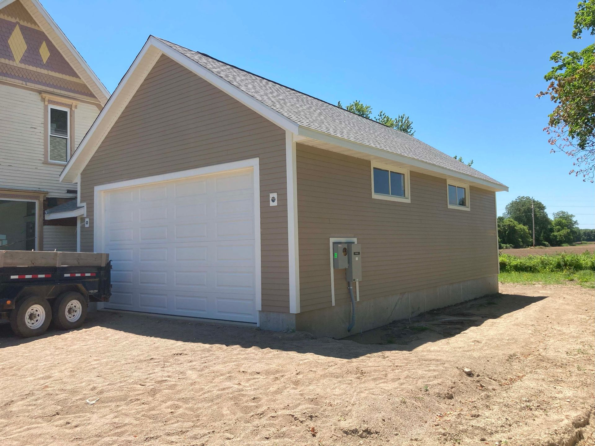 Beige garage with a white door next to an older home on a sunny day.
