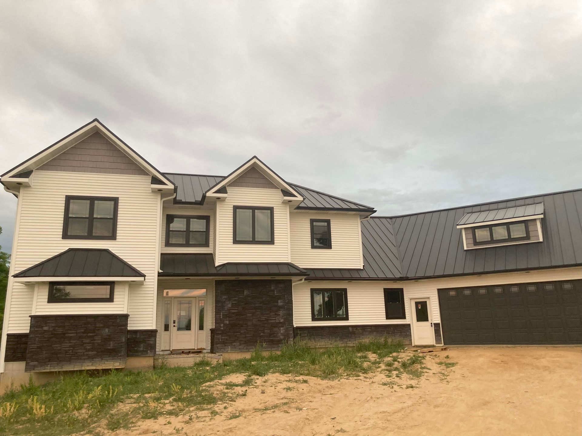 Two-story house under construction with white siding, black roof, and dark windows, against a cloudy sky.