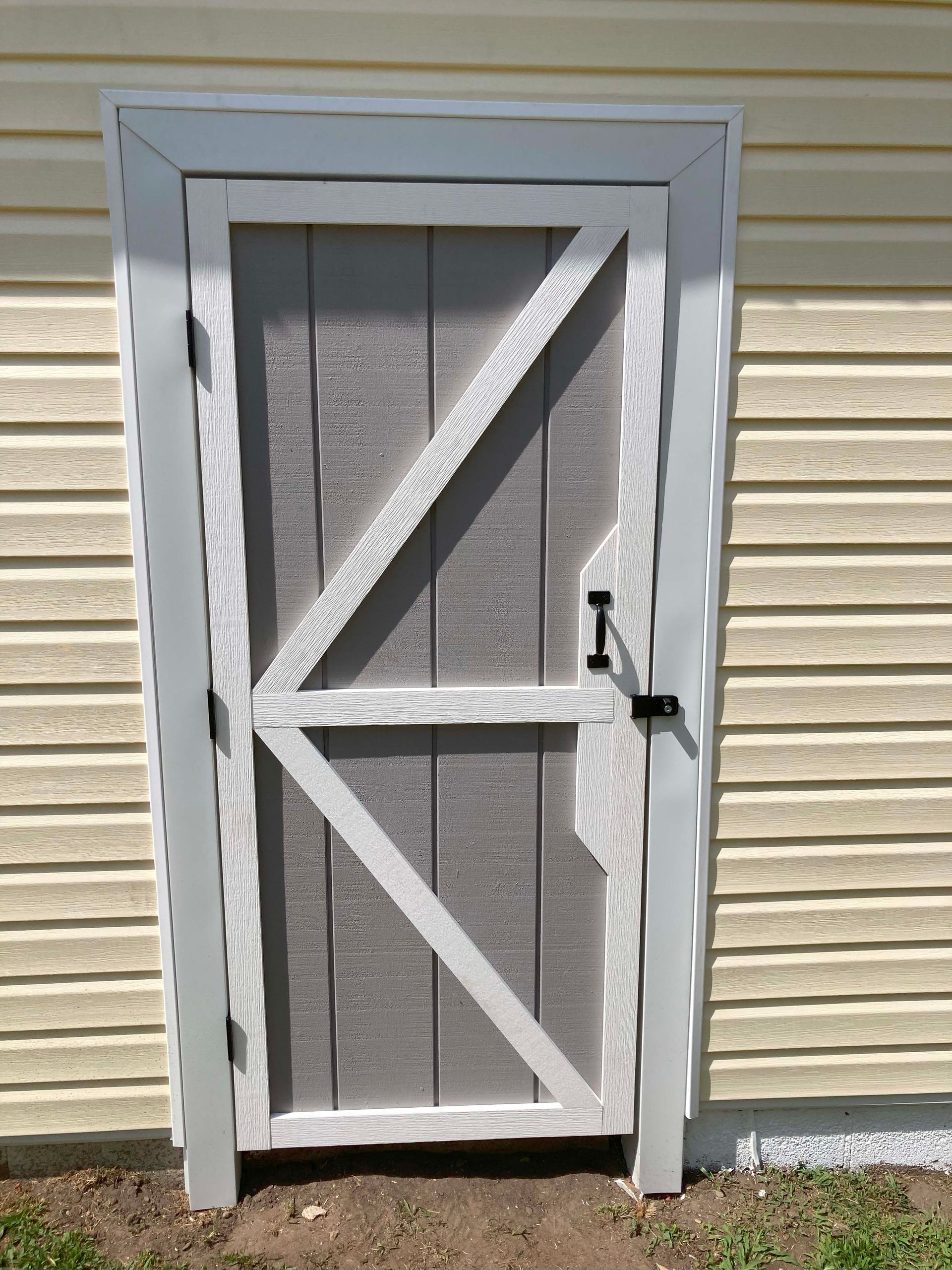White wooden screen door with diagonal brace, black latch, set in a light-yellow-sided building.