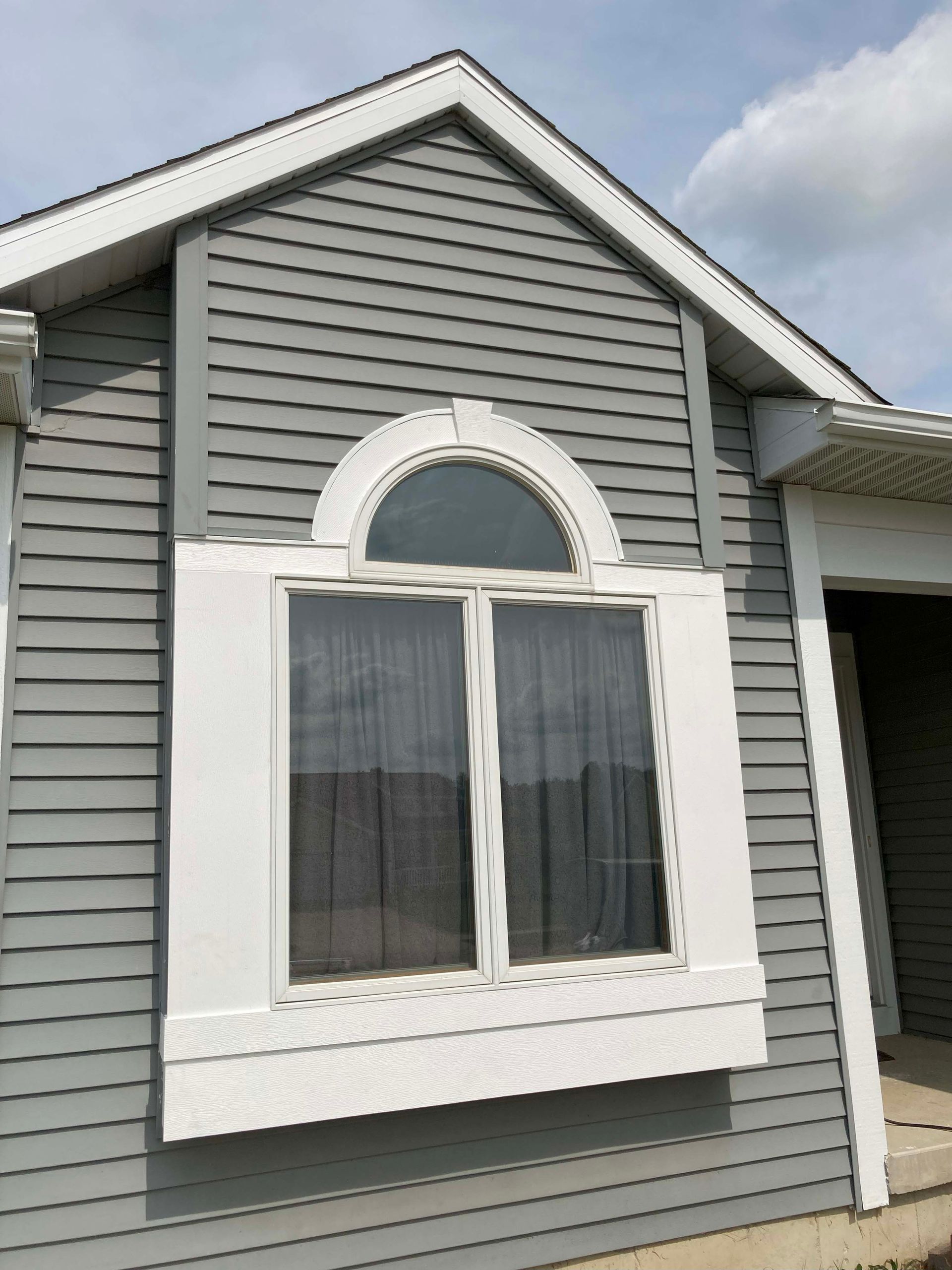 Gray house with white window trim and arched window on a sunny day.