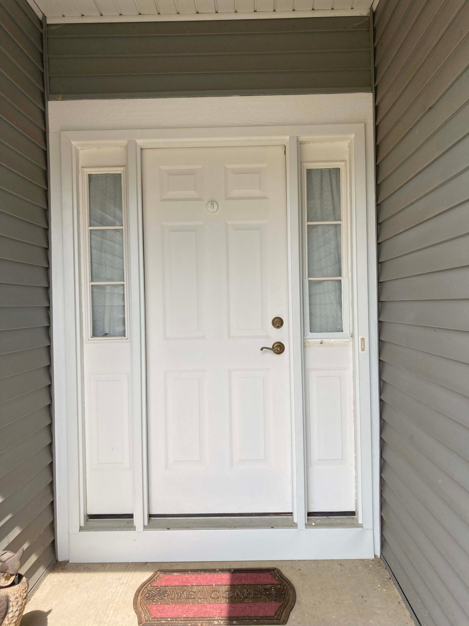 White front door with sidelights, red welcome mat.