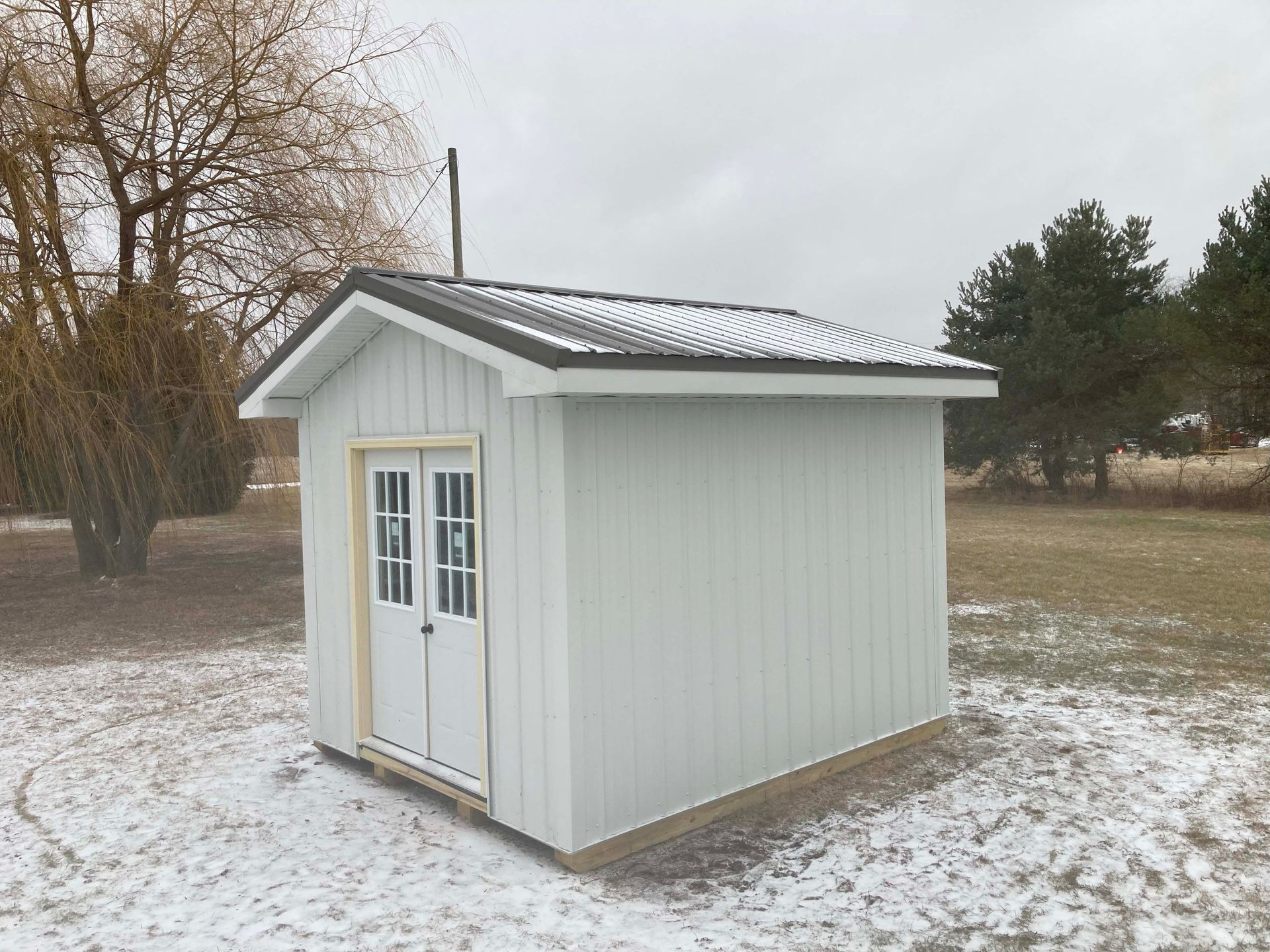 White shed with double doors, set in a snowy field. Overcast day.