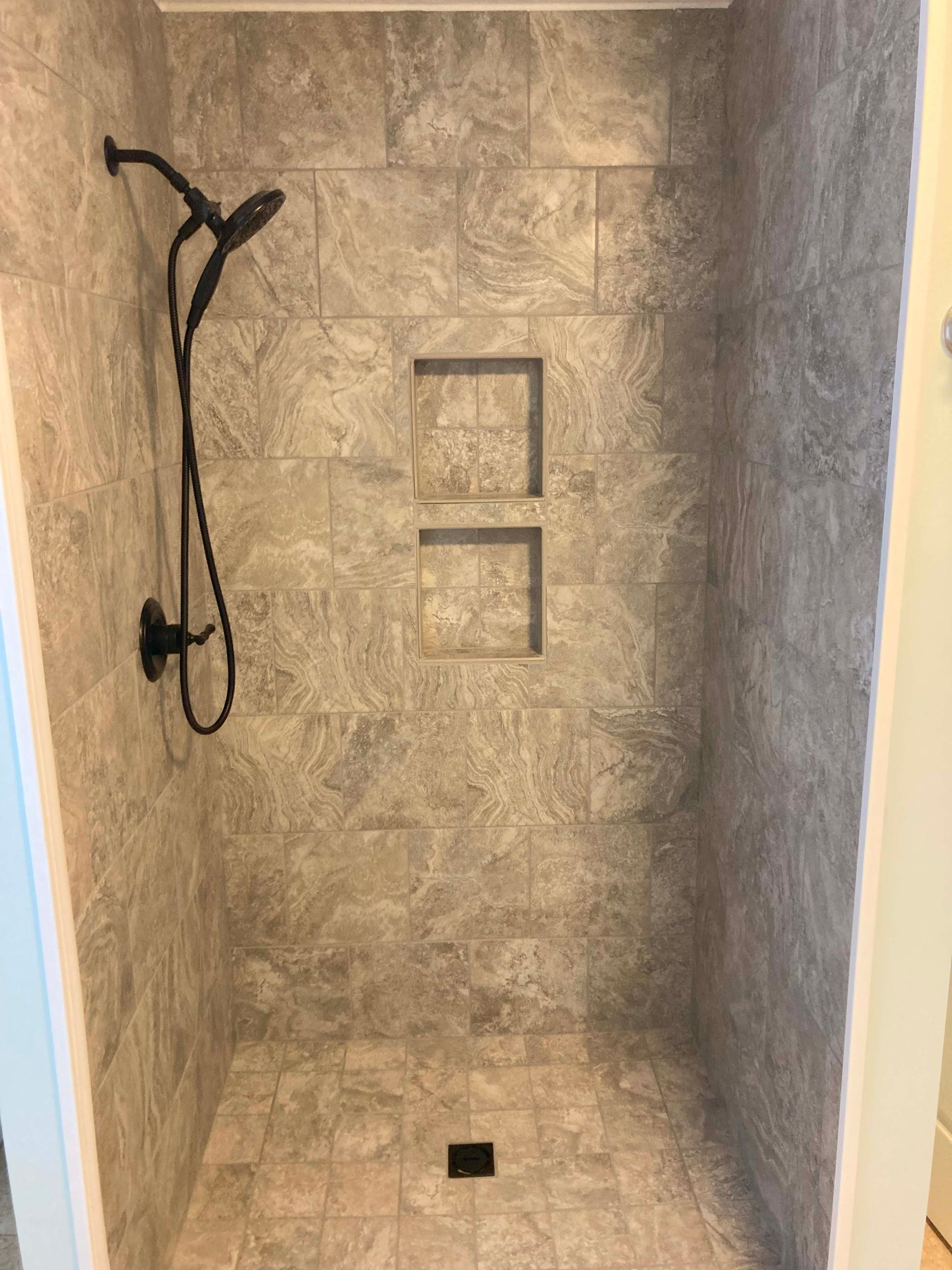 Gray tiled shower with black fixtures and two built-in shelves.