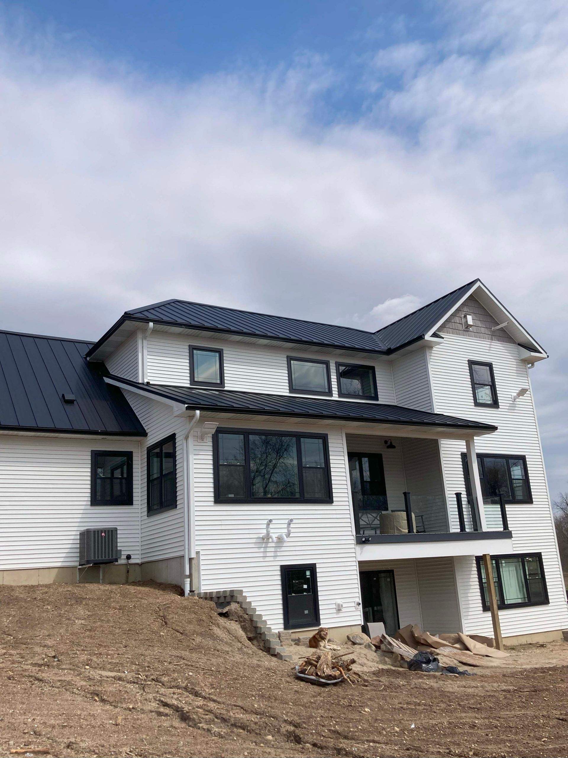 White house with black roof and window frames, set against a cloudy sky.