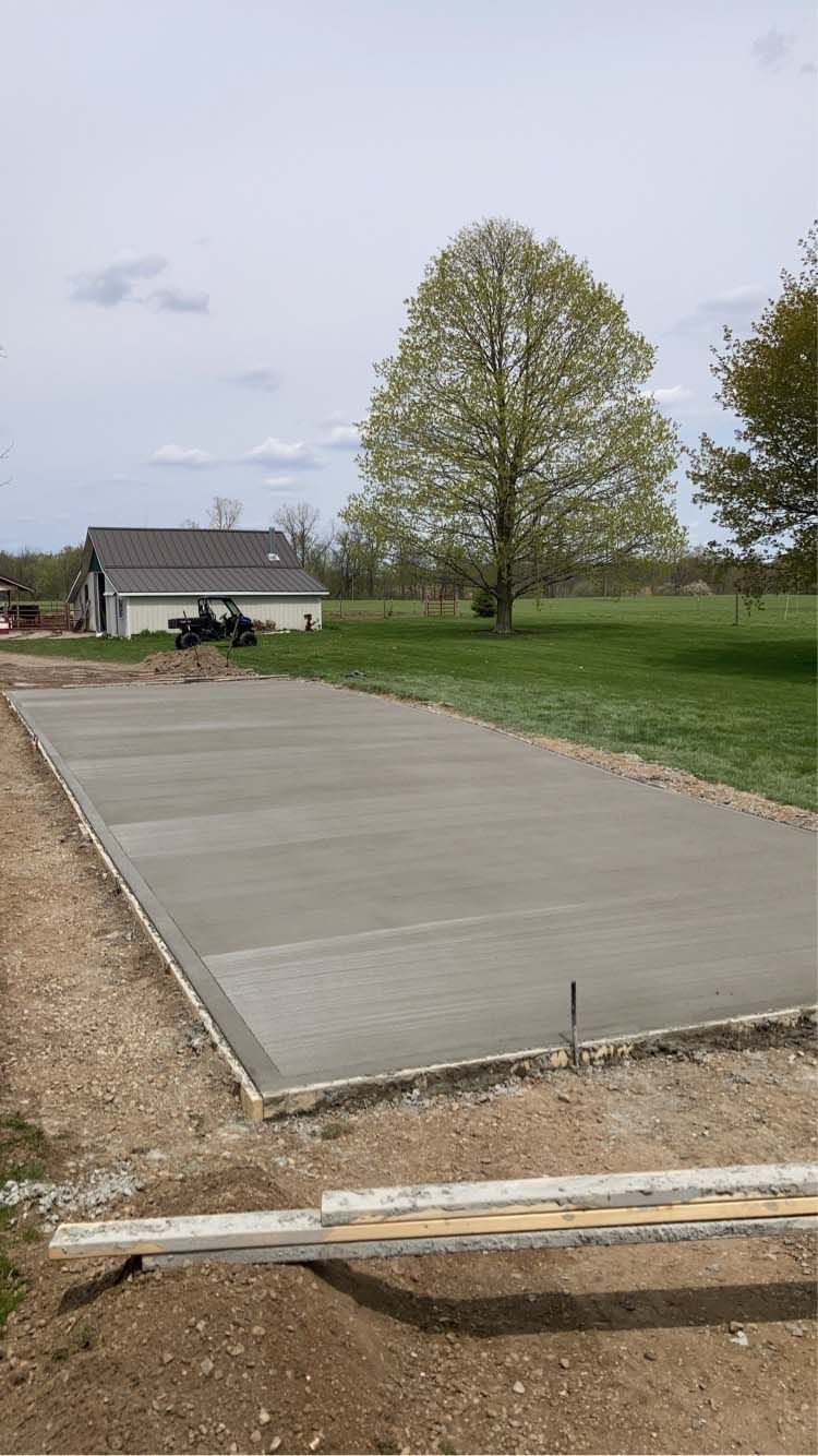 Newly poured concrete slab for a structure in a grassy area, small house in the background.