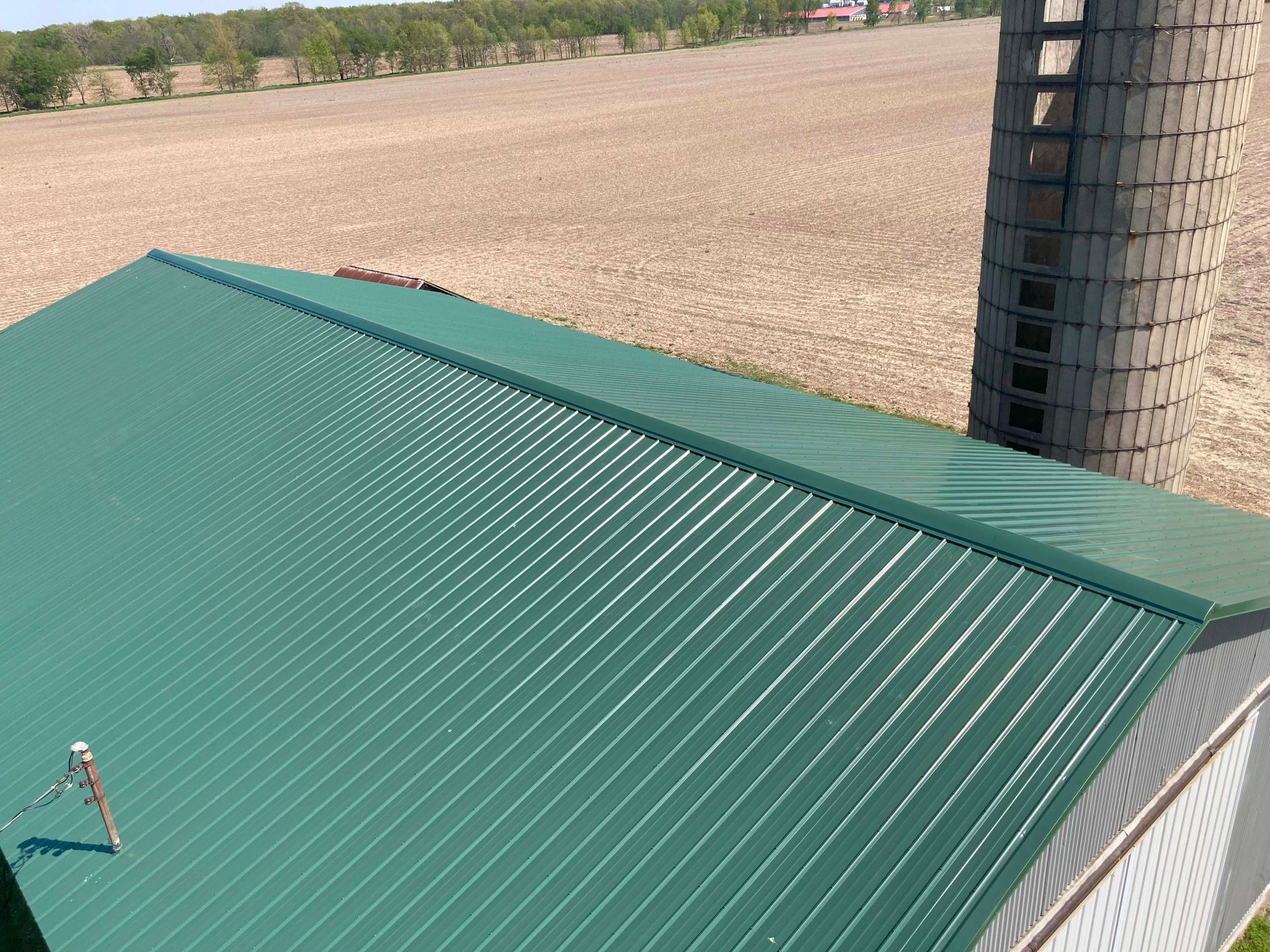 Green metal roof of a building with a silo in a field.