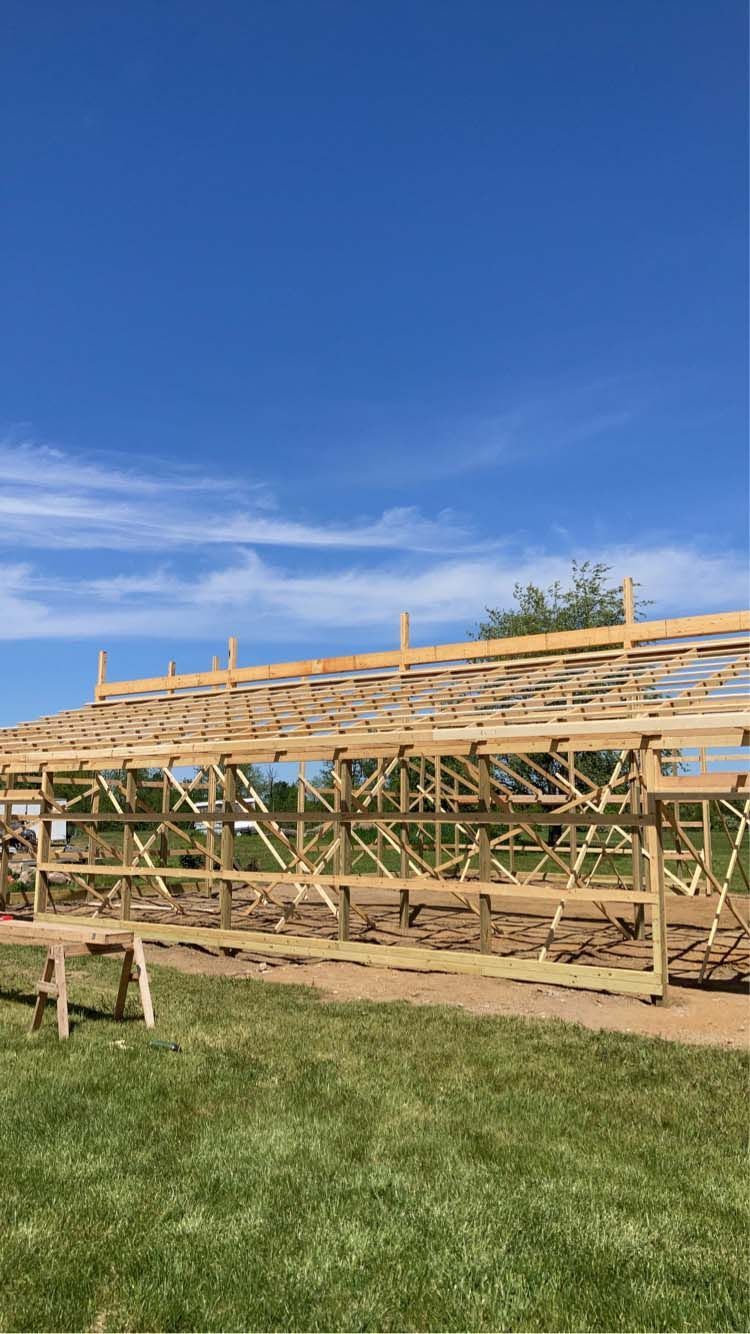 Wooden structure under construction against a blue sky, in a grassy field.