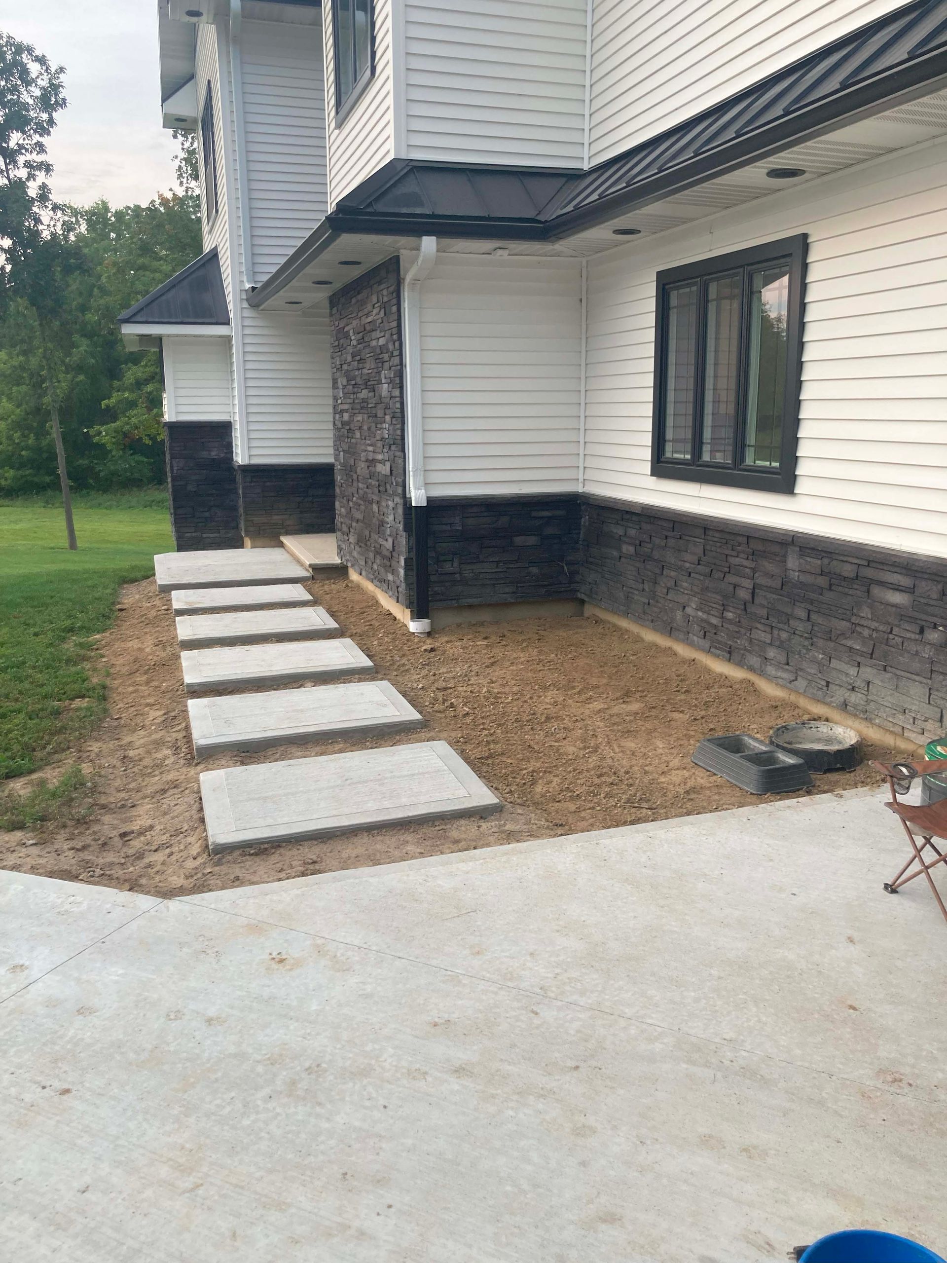 Concrete walkway leading to a house with black stone accents and white siding.