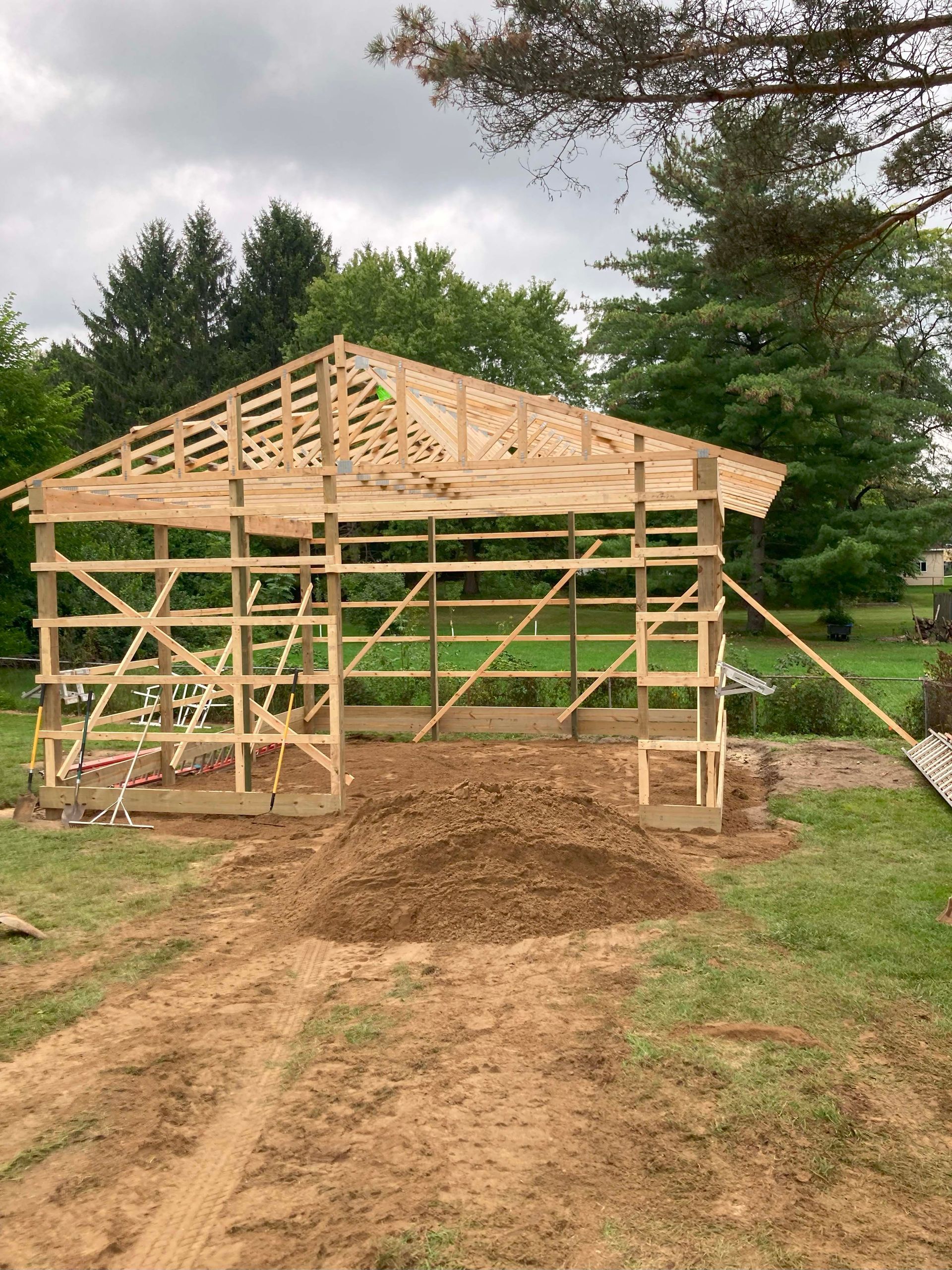 Wooden building frame under construction in a yard, with dirt pile and green grass.