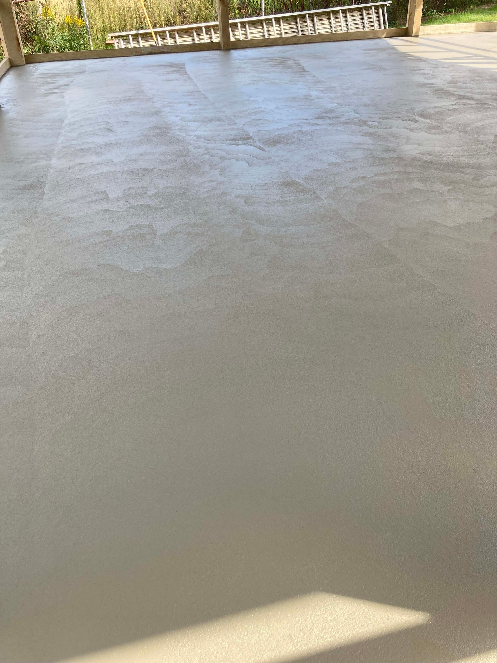 Gray concrete patio, smooth surface, with a wooden beam and ladder in the background.