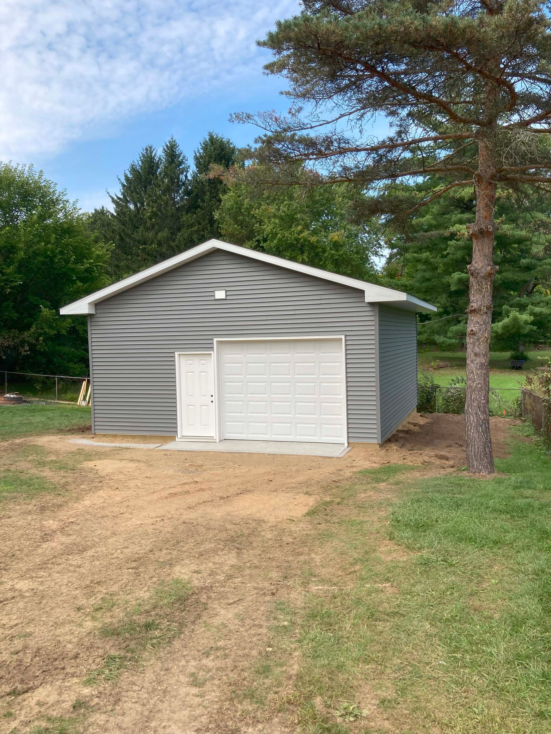 Gray metal garage with white door and garage door in a grassy area.