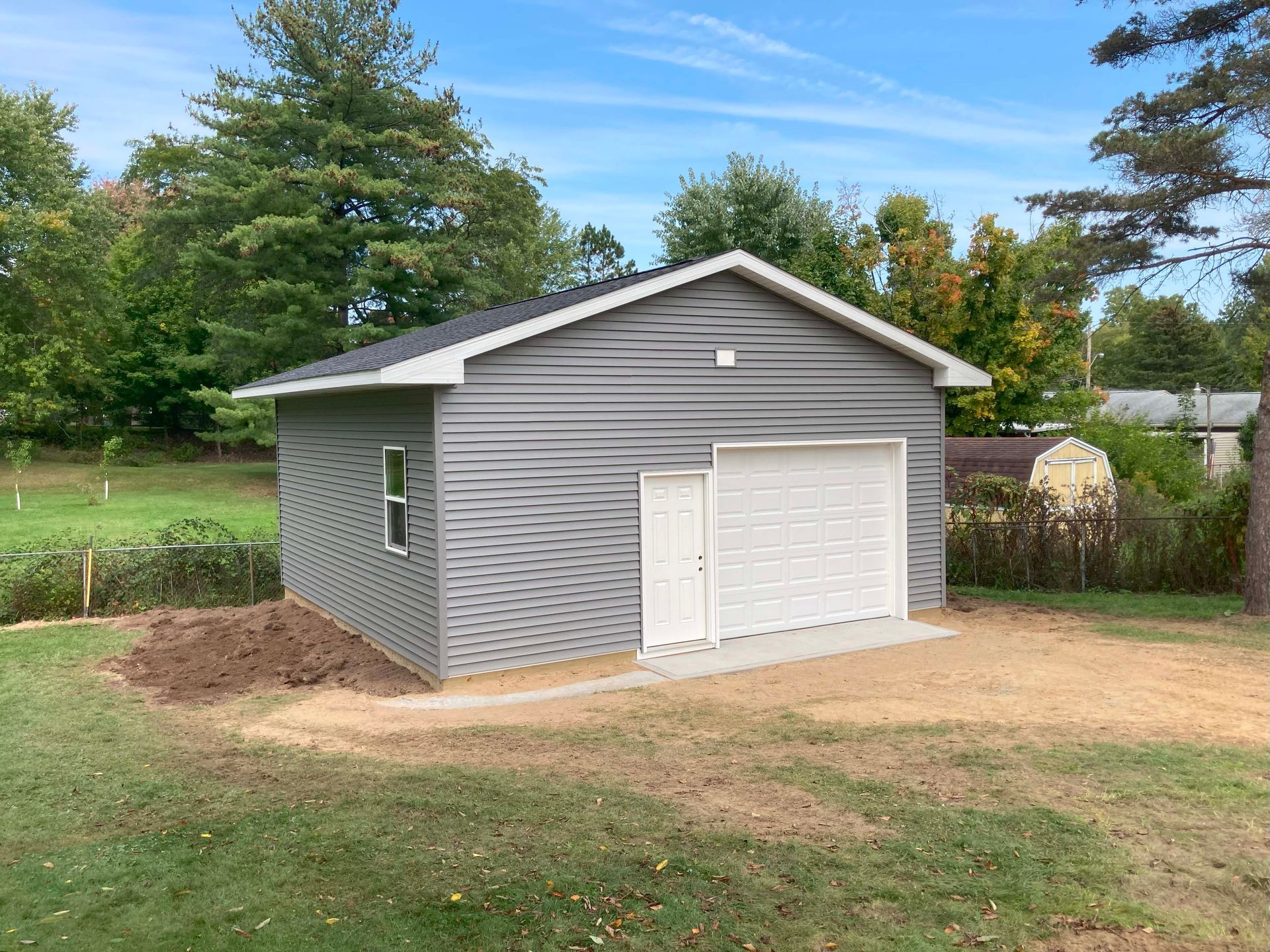 Gray-sided garage with white door and trim, on a concrete pad, set in a grassy yard.